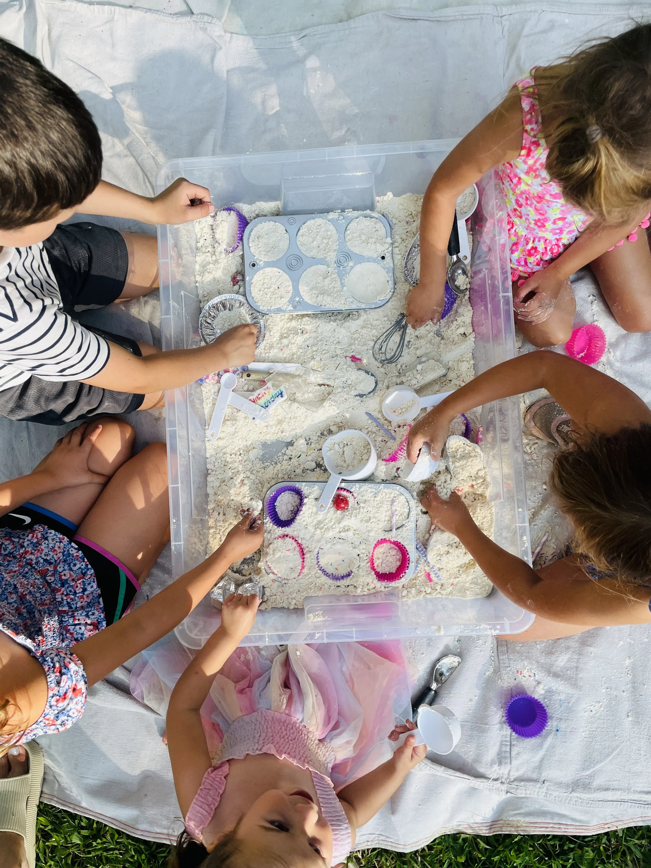 Children playing and making shapes in a sandbox with sand toys and molds.