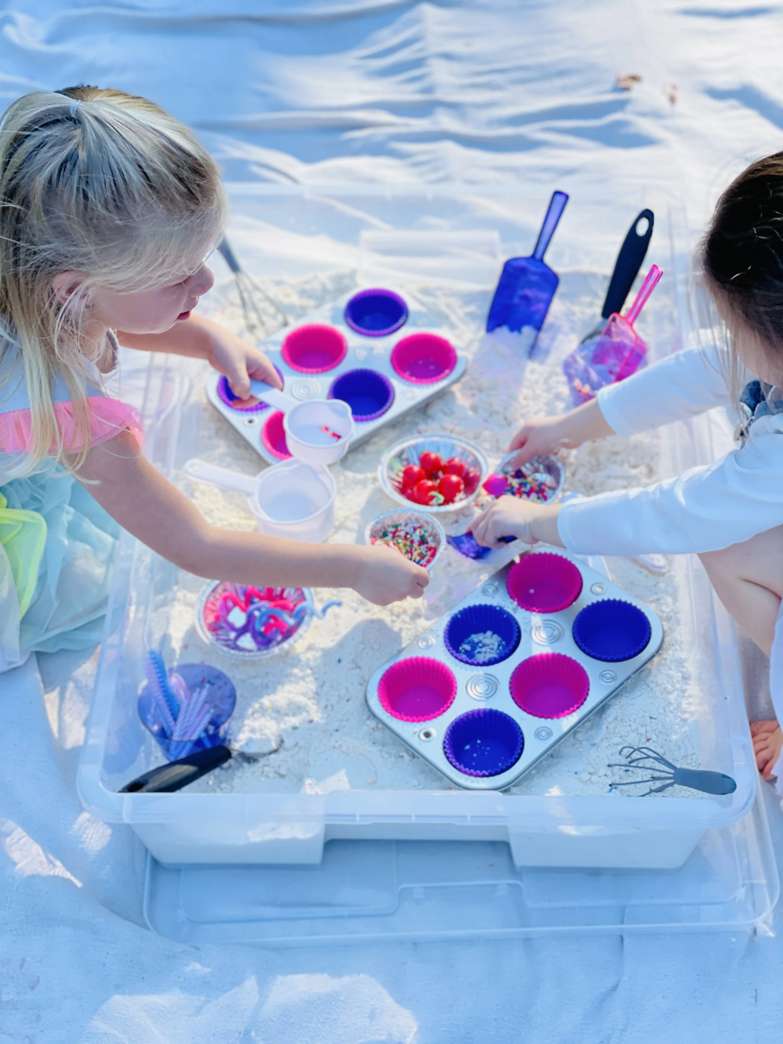 Two children on a snowy surface making colorful ice cubes with silicone molds, sprinkles, and toppings.