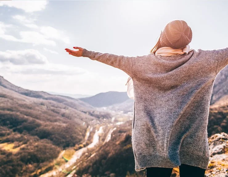 Person standing on a mountain overlooking a river valley with arms outstretched