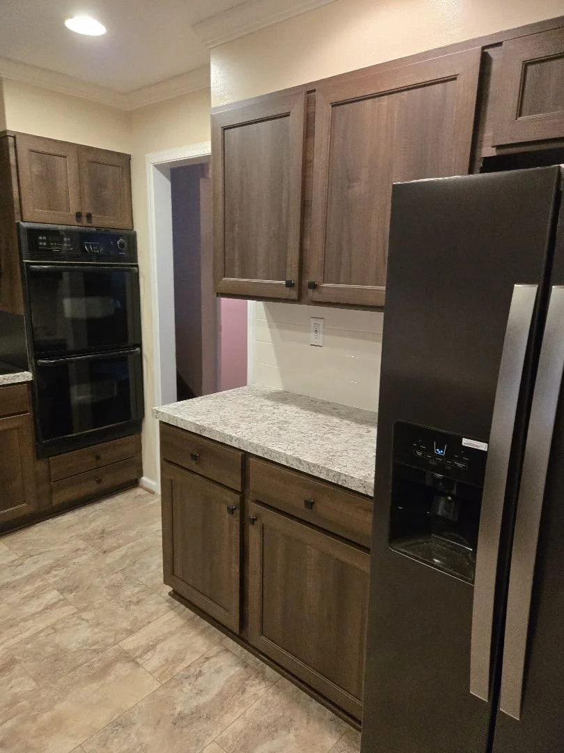 Kitchen with wooden cabinets, black double oven, granite countertop, and black side-by-side refrigerator near a doorway.