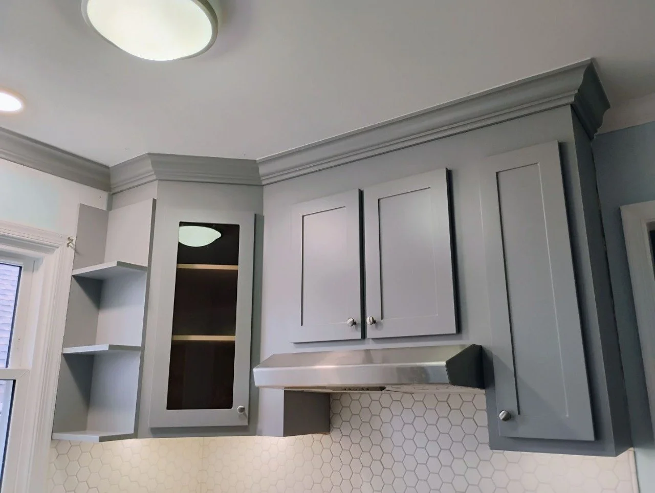 Gray kitchen cabinets with white hexagonal tile backsplash and a stainless steel range hood.