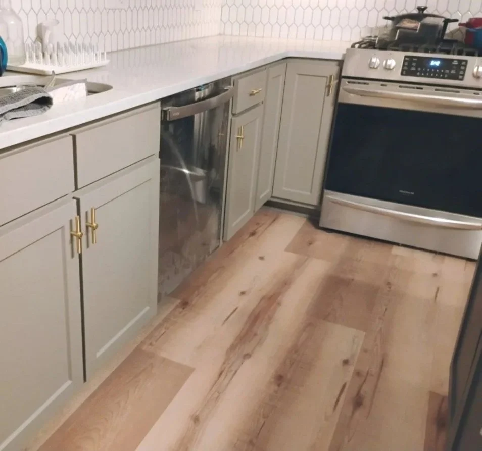 Kitchen with gray cabinets, white countertop, stainless steel dishwasher, gas stove, and wooden floor.