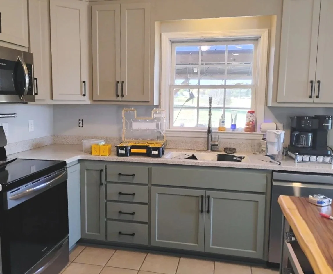 Kitchen with light green cabinets, a window above the sink, and various small appliances and tools on the counters.