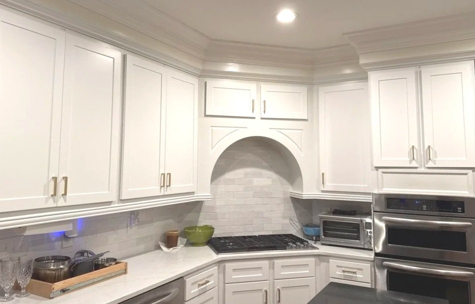 White kitchen cabinets with gold handles, a built-in oven, microwave, and a stovetop, with a white backsplash and countertop.