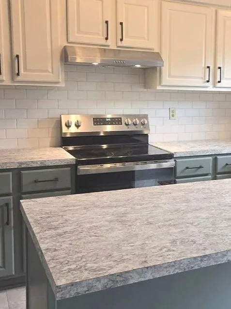 Kitchen with granite countertops, white subway tile backsplash, beige upper cabinets and green lower cabinets, and a stainless steel stove with range hood.