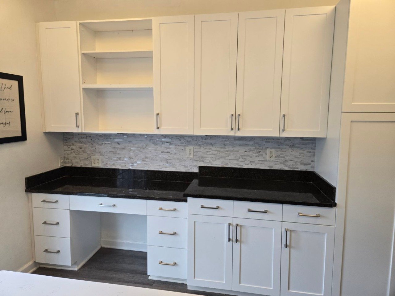White kitchen cabinets with black countertops, a textured gray backsplash, and multiple drawers and cabinets, some open shelving in the upper cabinets.
