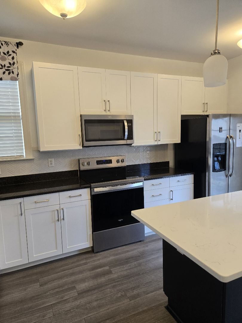 Modern kitchen with white cabinets, black countertops, stainless steel appliances including a microwave, oven, and refrigerator, and a white island with a dark base.