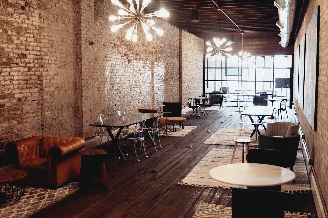Interior of a modern, industrial-style lounge with exposed brick walls, wooden floors, contemporary lighting fixtures, and various seating arrangements for office and business use, in Lynchburg, Va.