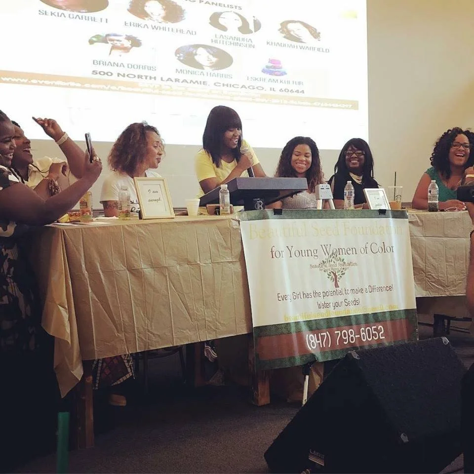 Women sitting at a panel discussion for the Beautiful Seed Foundation for Young Women of Color, with a banner displaying the organization's name and contact details, in Chicago.