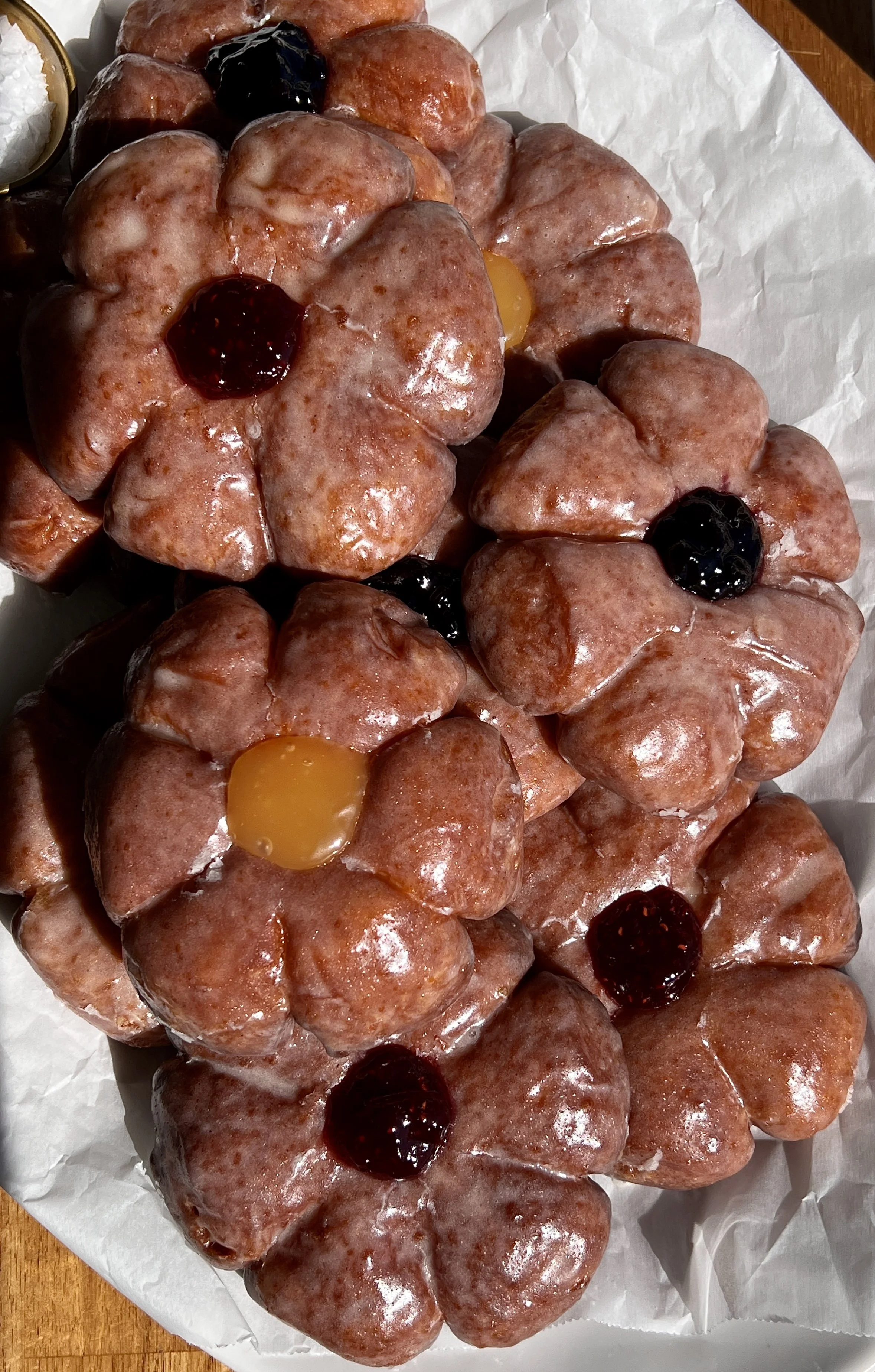 Flower donuts coated in vanilla bean glaze and filled with fruit preserves, served warm.