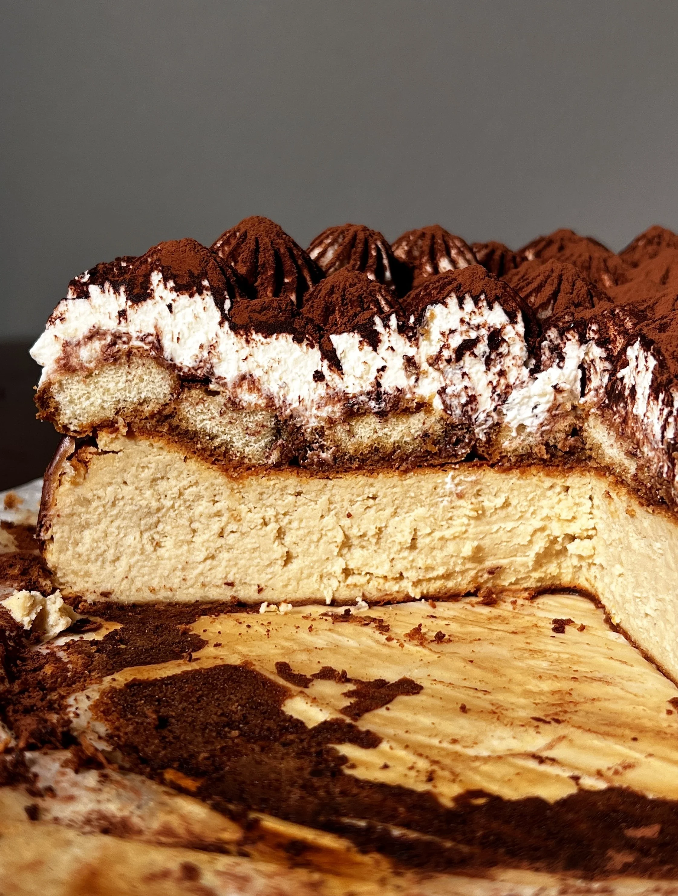 Tiramisu basque cheesecake topped with espresso-soaked ladyfingers, creamy mascarpone layer, and a generous dusting of cocoa powder.