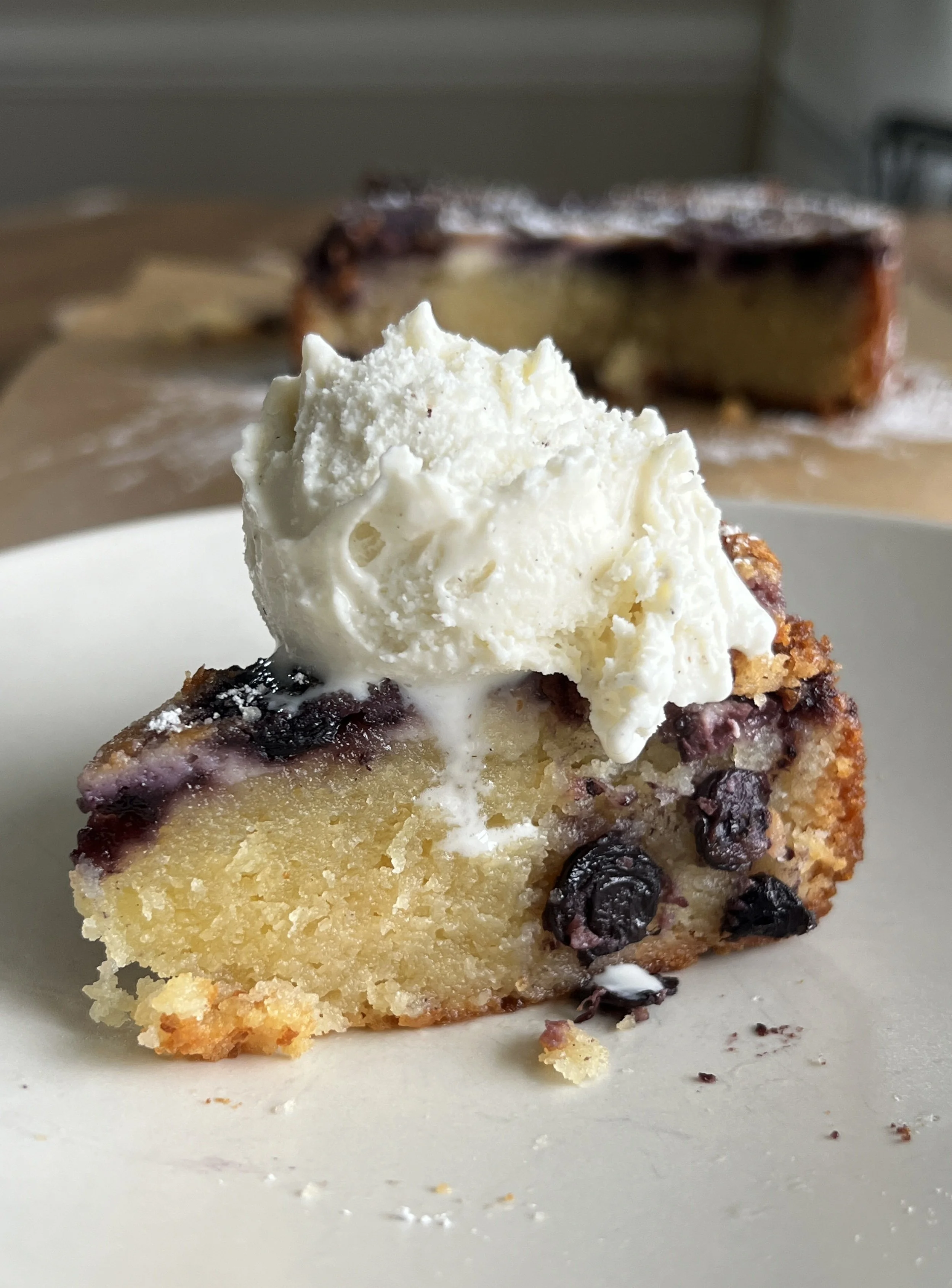 Close-up of a Mini Blueberry Gooey Butter Cake topped with fresh blueberries and a golden-brown crust, served on a white plate. This delectable dessert is bursting with juicy blueberries and a rich, gooey center, making it a perfect treat for satisfy