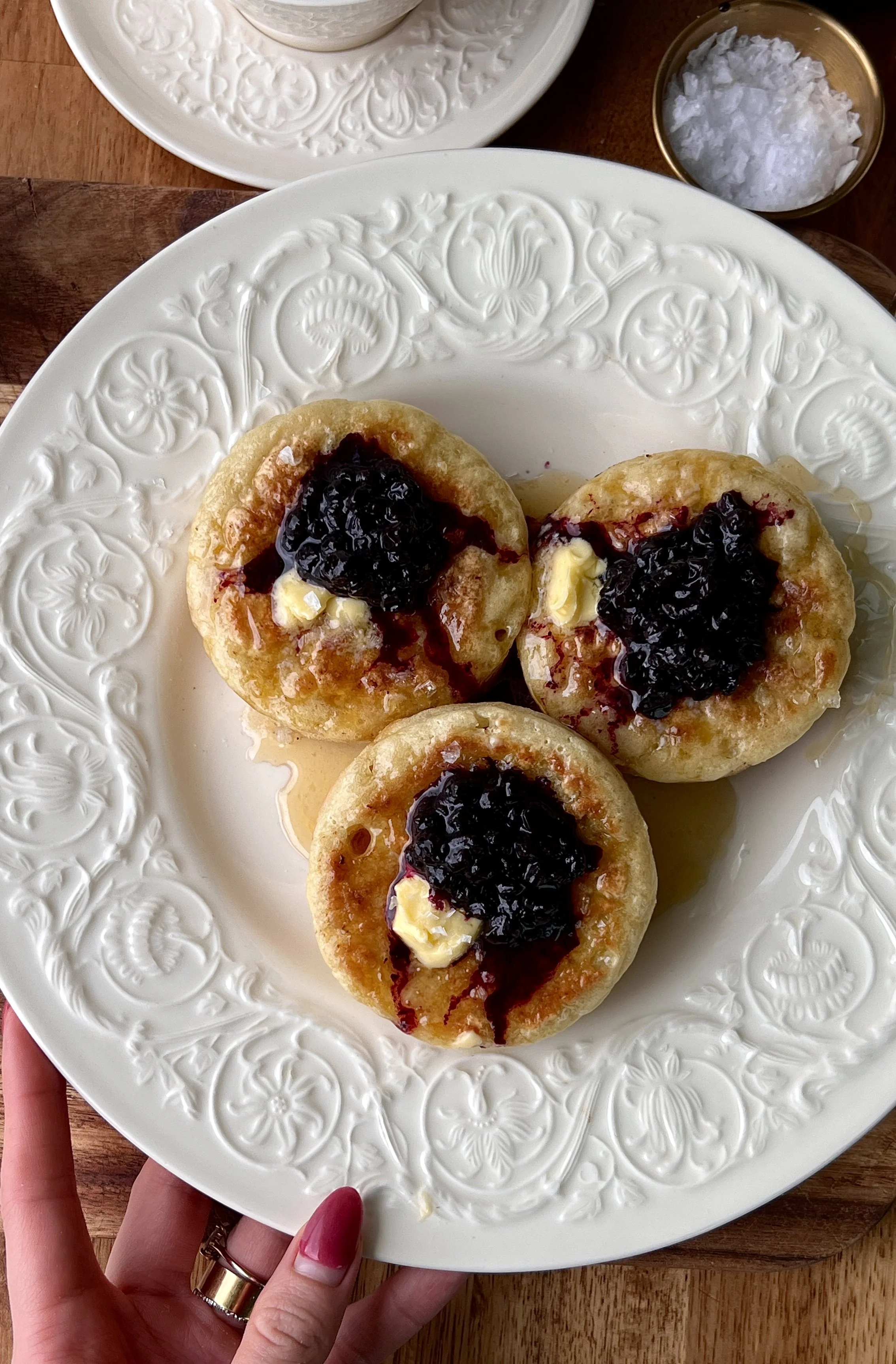 Stack of golden homemade crumpets served with blueberry compote, a drizzle of honey, and a hot cup of coffee.