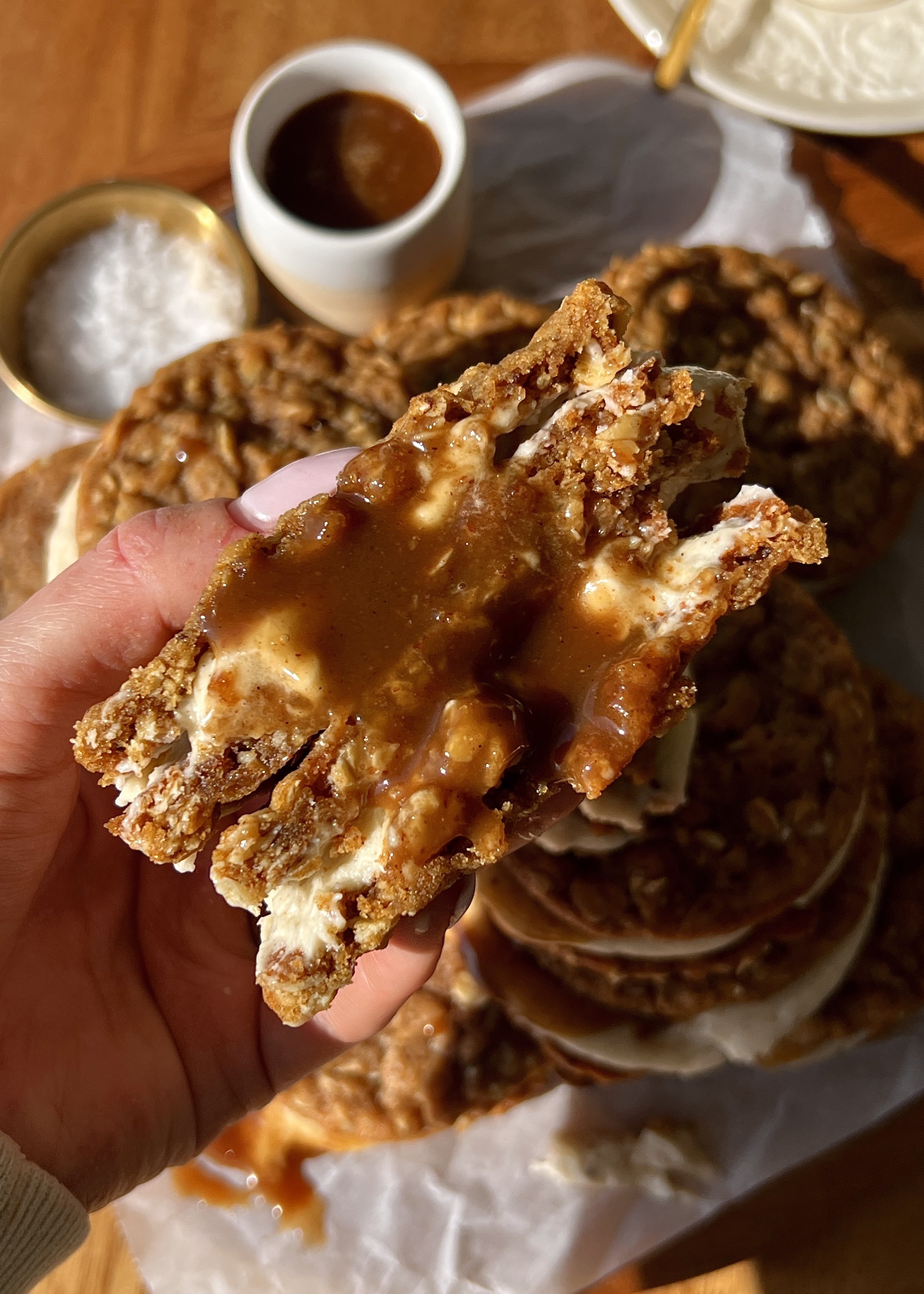 Close-up of a brown butter sweet potato oatmeal cream pie showing the soft and chewy spiced sweet potato oatmeal cookie with lush brown butter cream cheese filling and salted maple caramel in the middle.