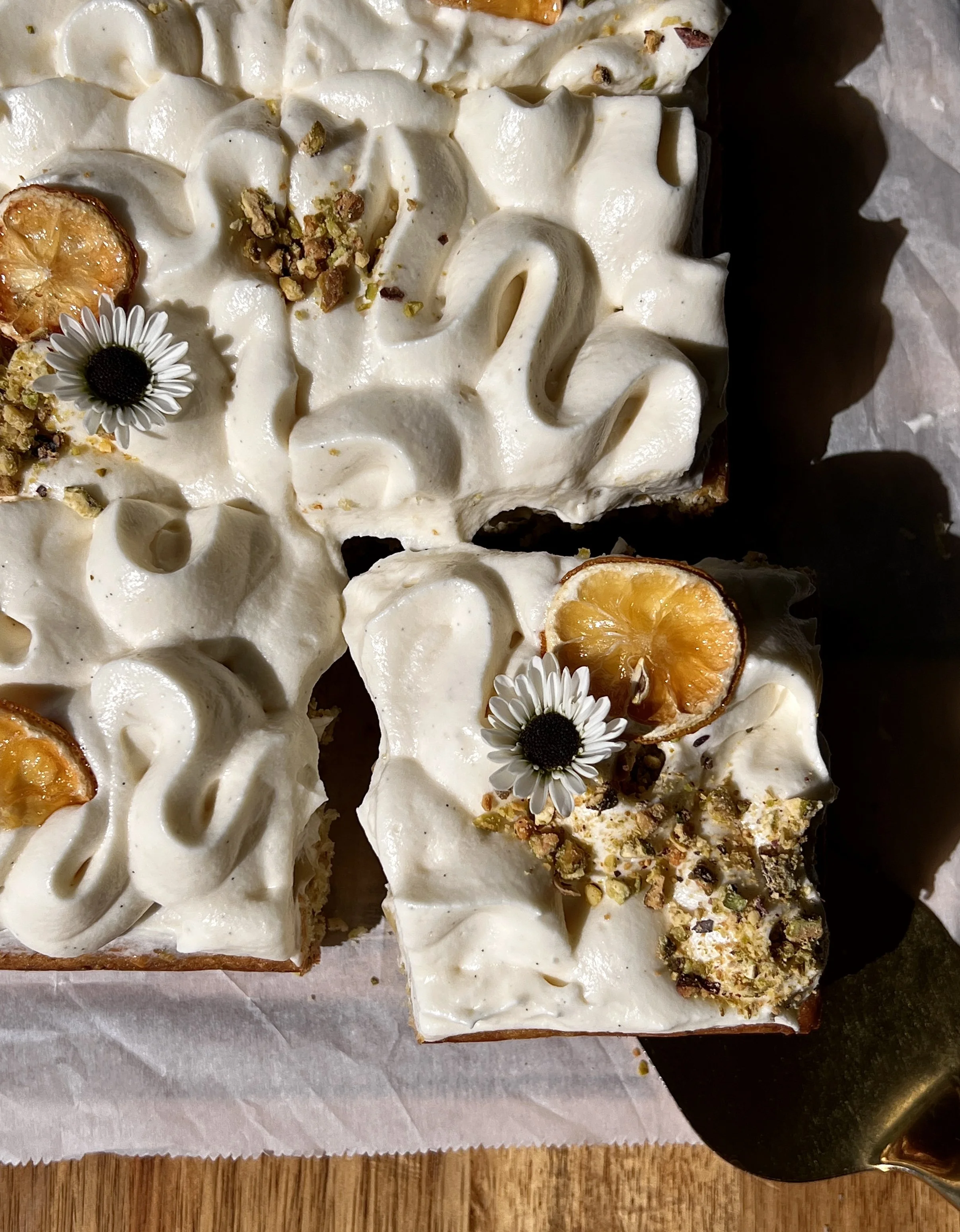 Slice of lemon curd pistachio cake with cream cheese frosting and a sprinkle of chopped pistachios.