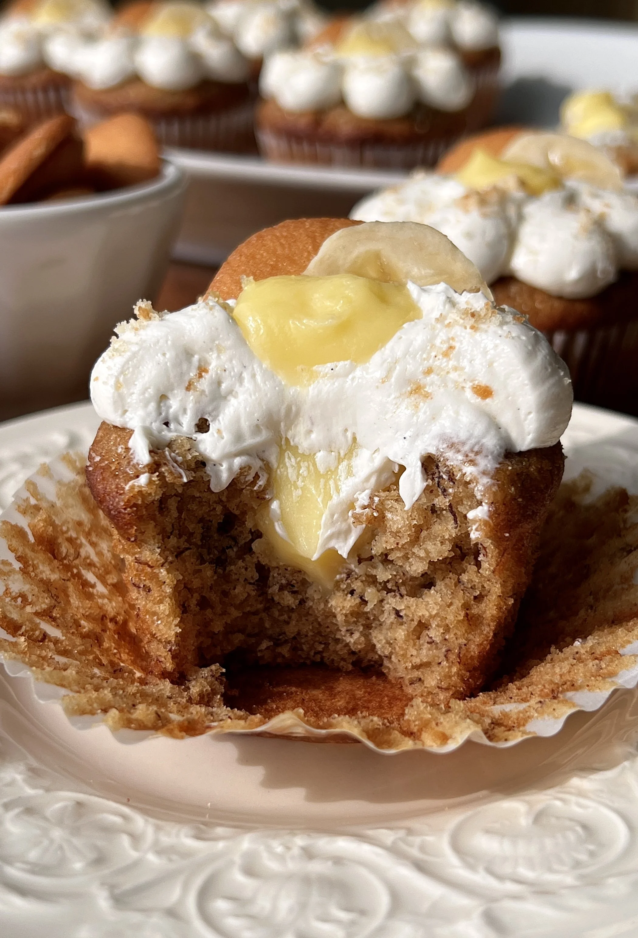 Brown butter banana pudding cupcake with a bite taken out showing the classic vanilla pudding filling inside and whipped buttercream on top.