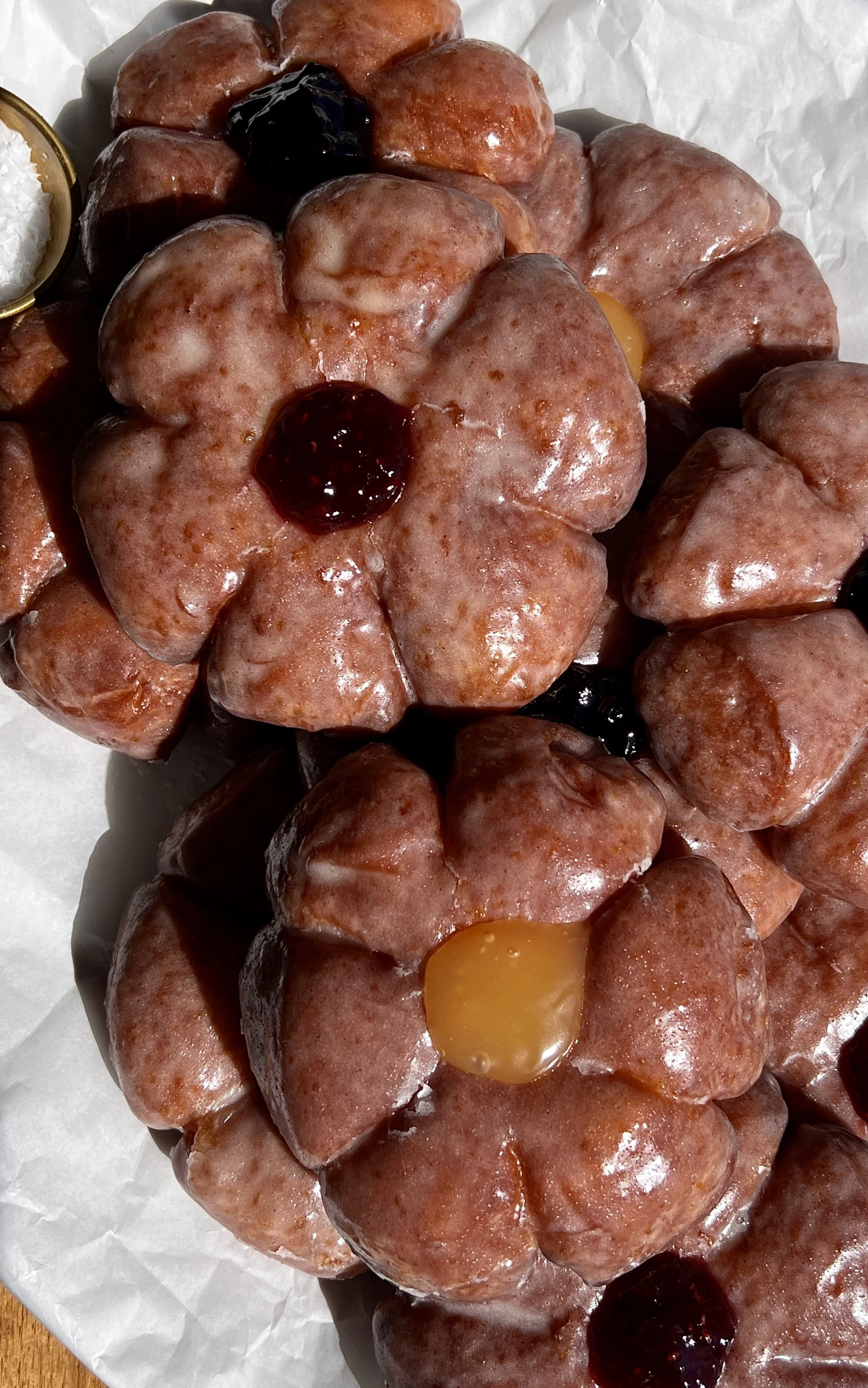 Flower donuts coated in vanilla bean glaze and filled with fruit preserves, served warm.