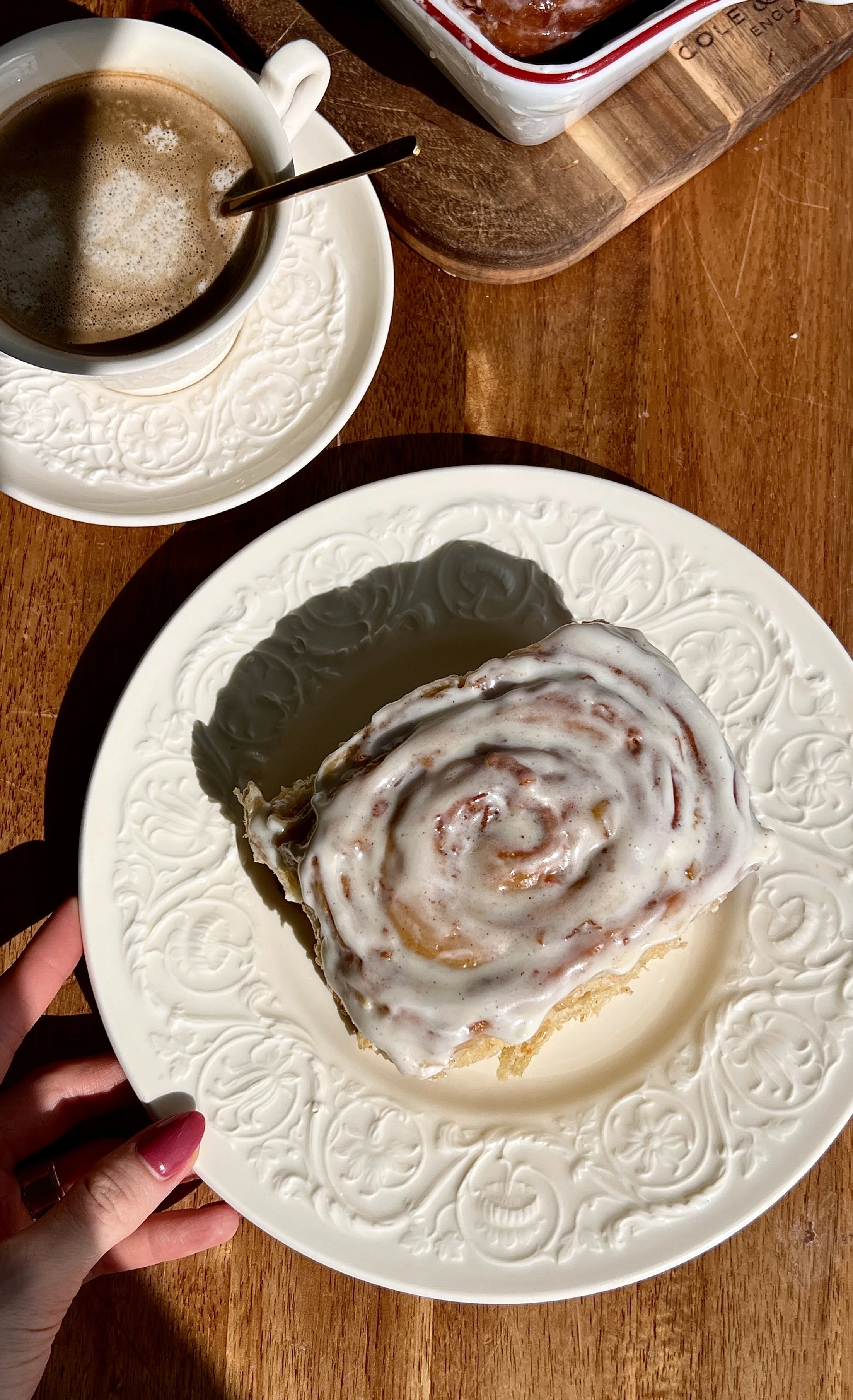 Warm carrot cake cinnamon rolls served with cream cheese frosting and a hot cup of coffee.