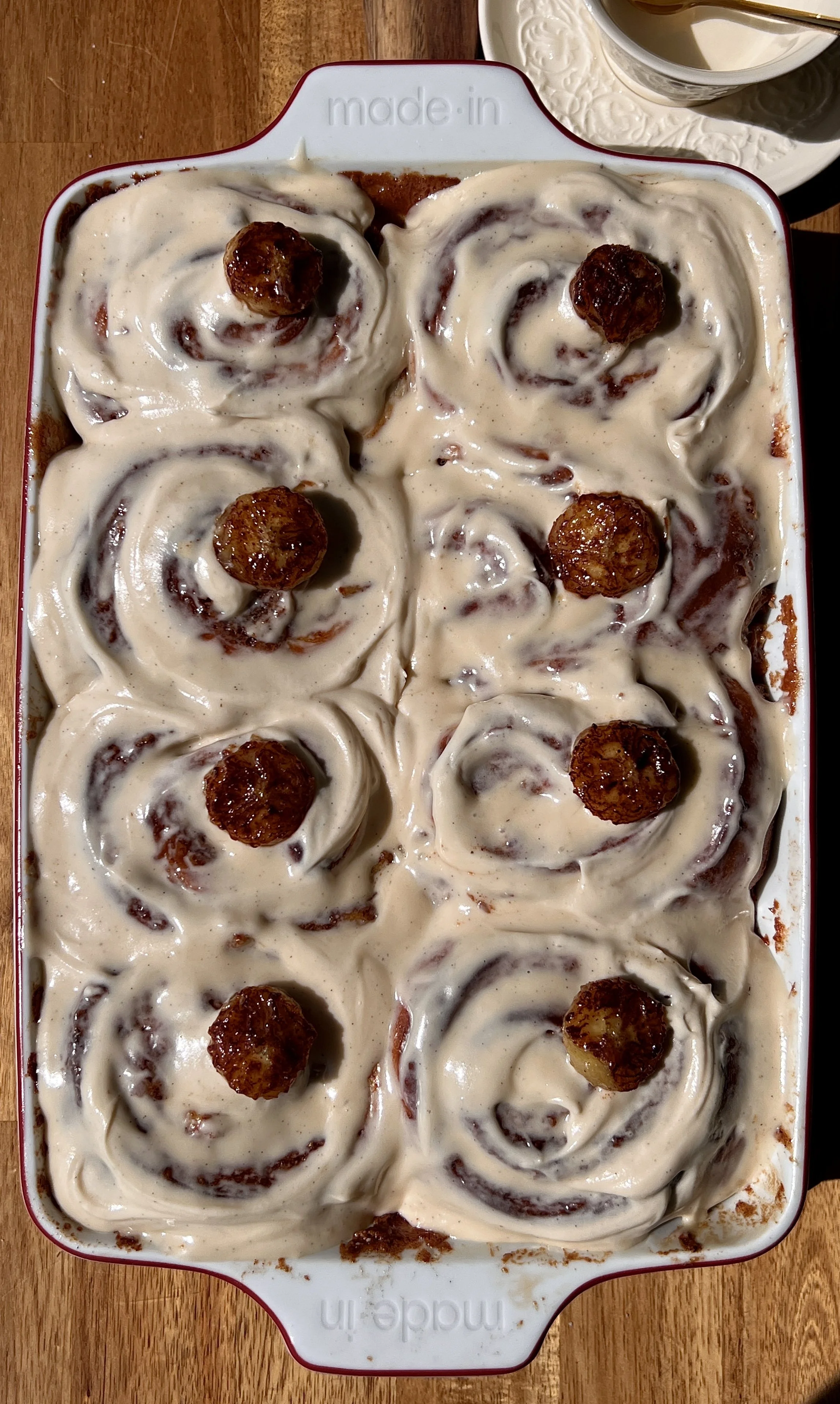 Pan of golden banana bread buttermilk cinnamon rolls with sticky caramelized edges topped with honey brown sugar cream cheese frosting melting into every swirl.