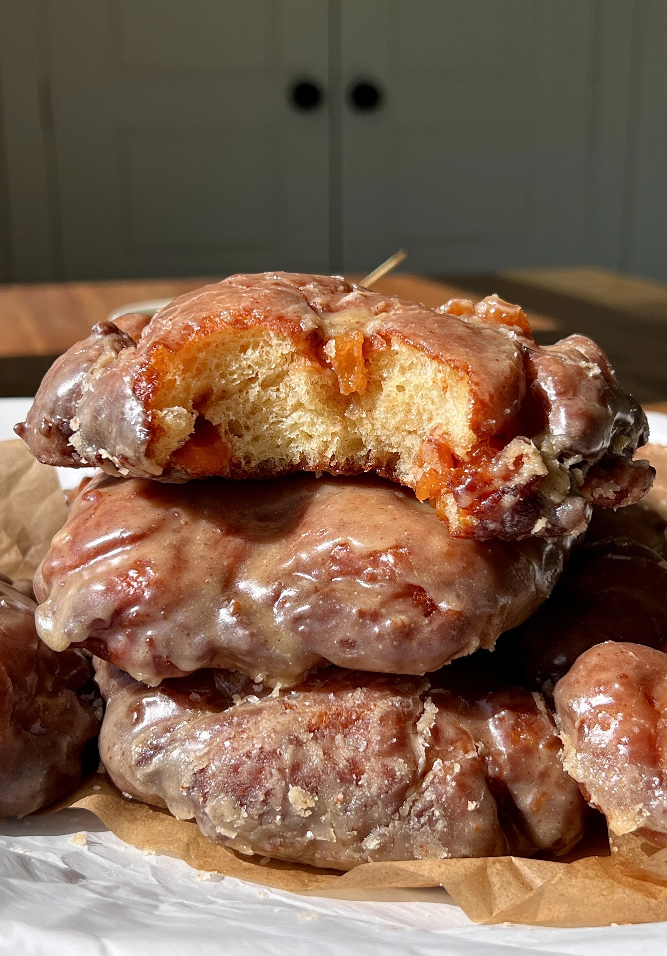 Peach fritter donut with a bite taken out showing the soft fluffy interior with warm gooey tart juicy peach filling throughout coated in a silky brown butter maple vanilla bean glaze.