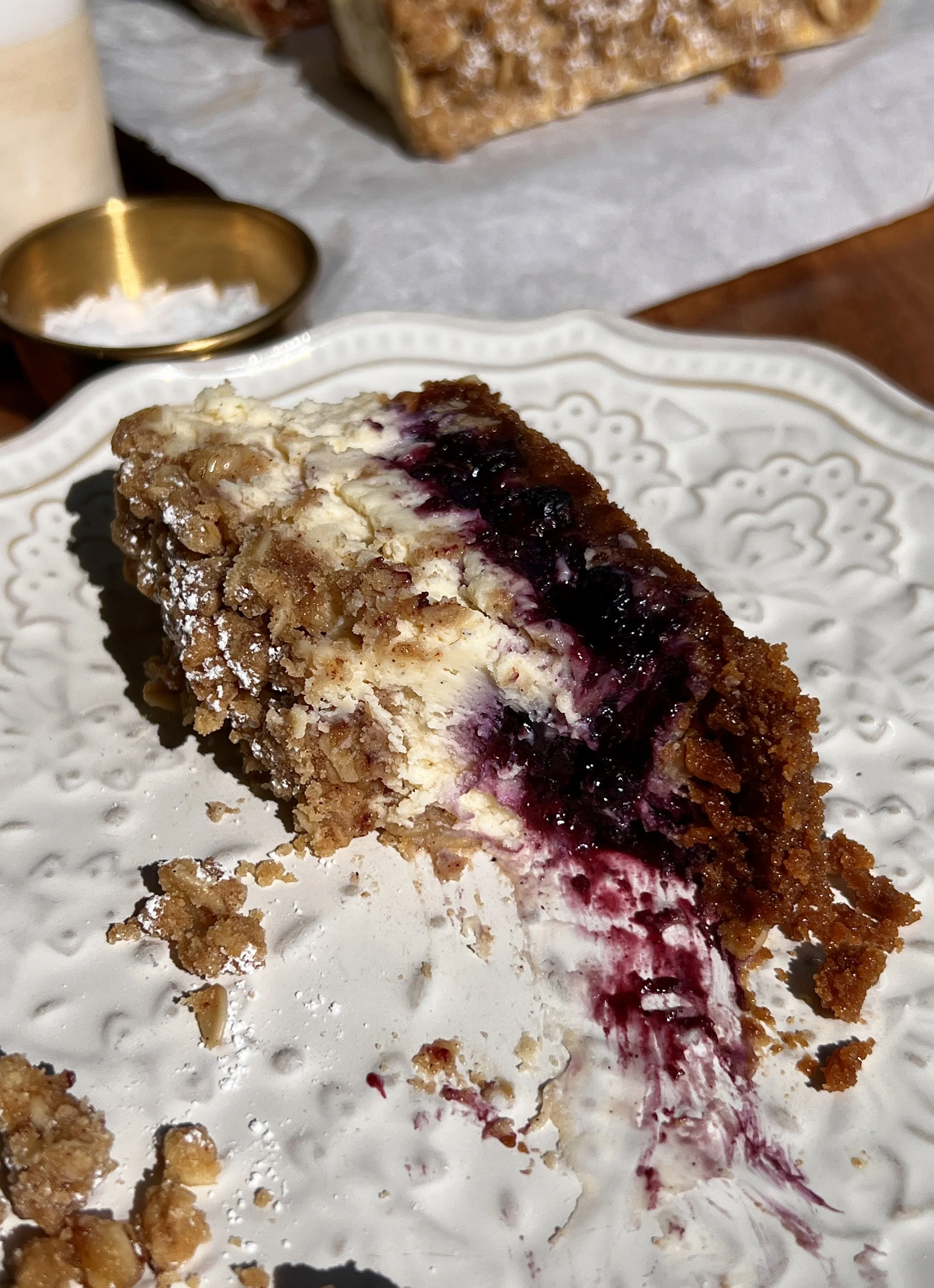 Blueberry crumble cheesecake bars with a buttery Biscoff cookie crust, tangy vanilla bean cheesecake filling, homemade blueberry compote, and golden crumble topping served on a plate.