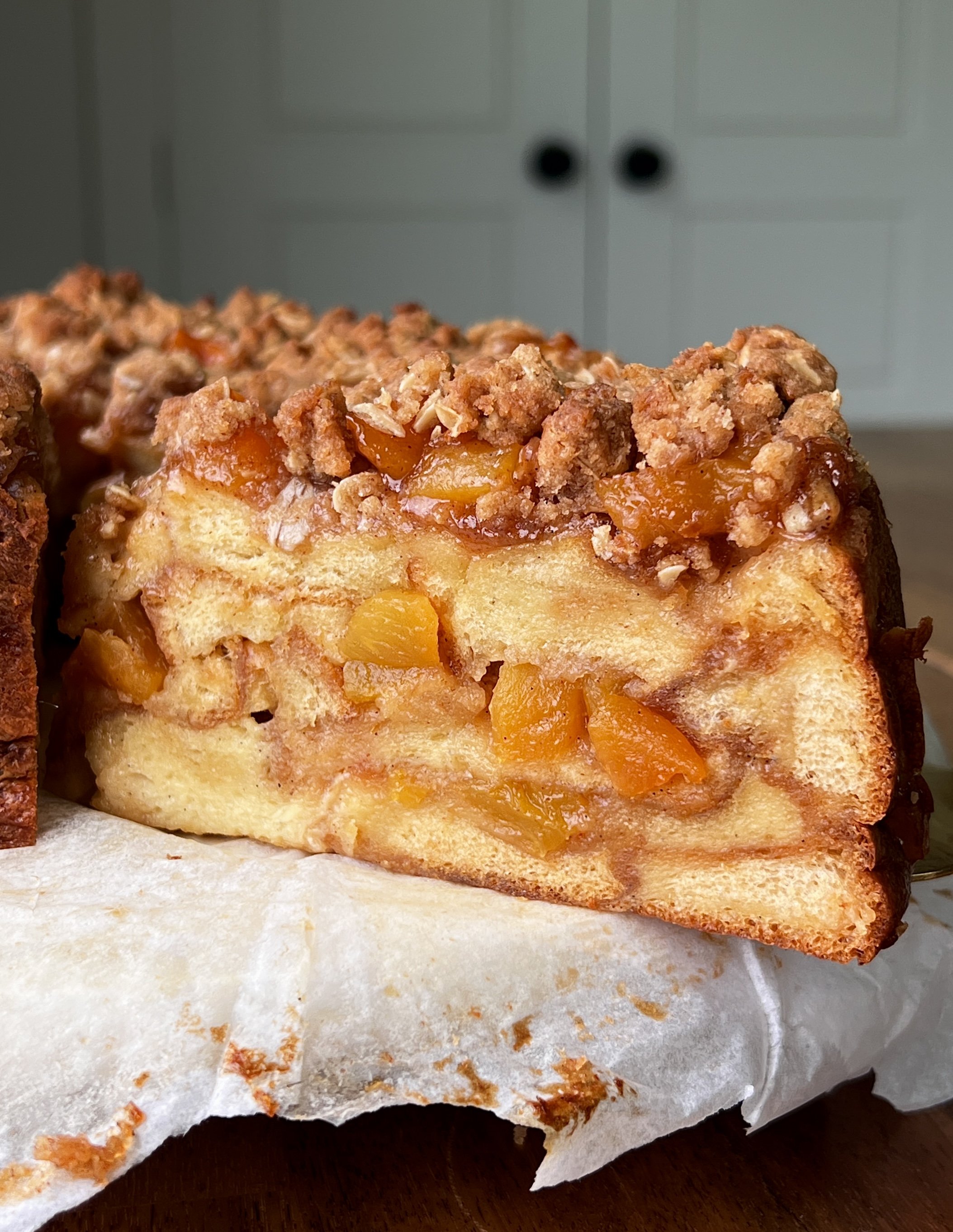 Close-up of peach cobbler buttermilk bread pudding showing the soft brioche bread soaked in vanilla bean buttermilk custard with a warm and gooey peach cobbler filling and golden oat streusel throughout.