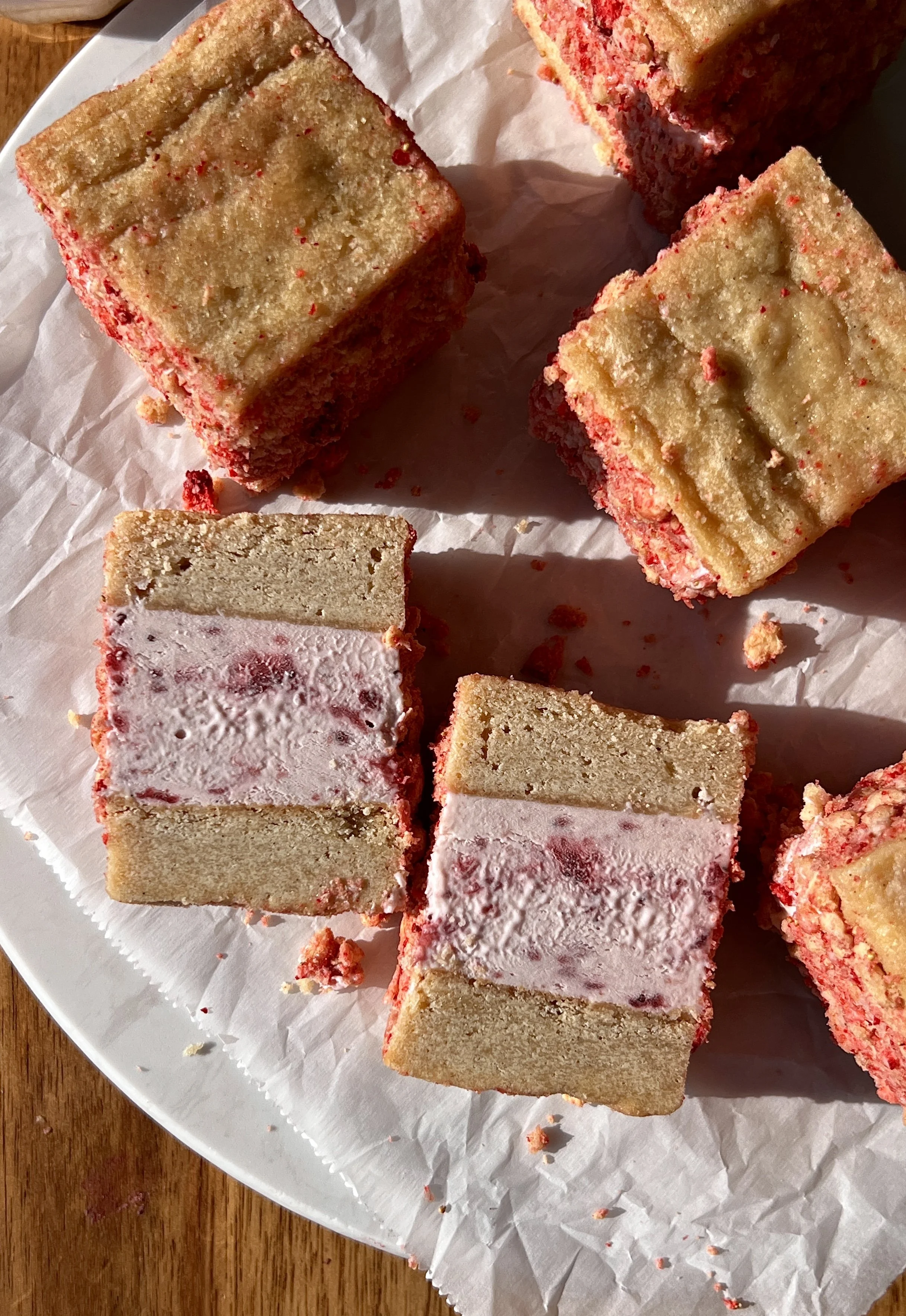 Close-up of a strawberry shortcake shortbread ice cream sandwich showing the soft buttery shortbread layers with rich and creamy homemade no-churn strawberry ice cream coated in a strawberry shortcake crunch coating throughout.