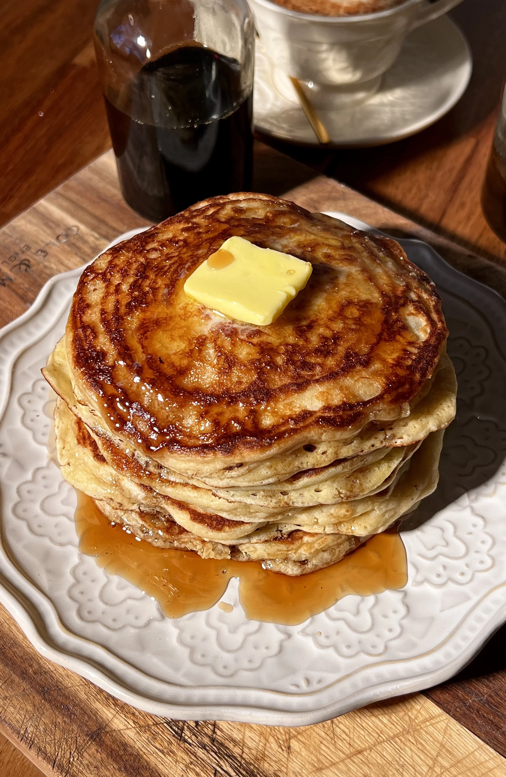 Classic buttermilk pancakes stacked high on a plate, soft and fluffy with golden edges, topped with butter and maple syrup, served alongside a warm maple brown butter latte.