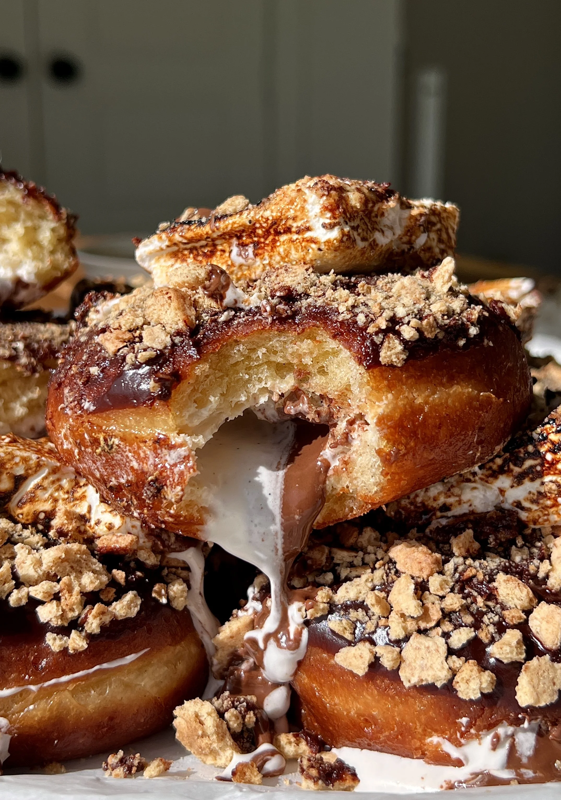 S'mores donut with a bite taken out showing the pillowy soft interior filled with light and smooth marshmallow buttercream and Nutella inside with chocolate ganache and toasted marshmallow on top.