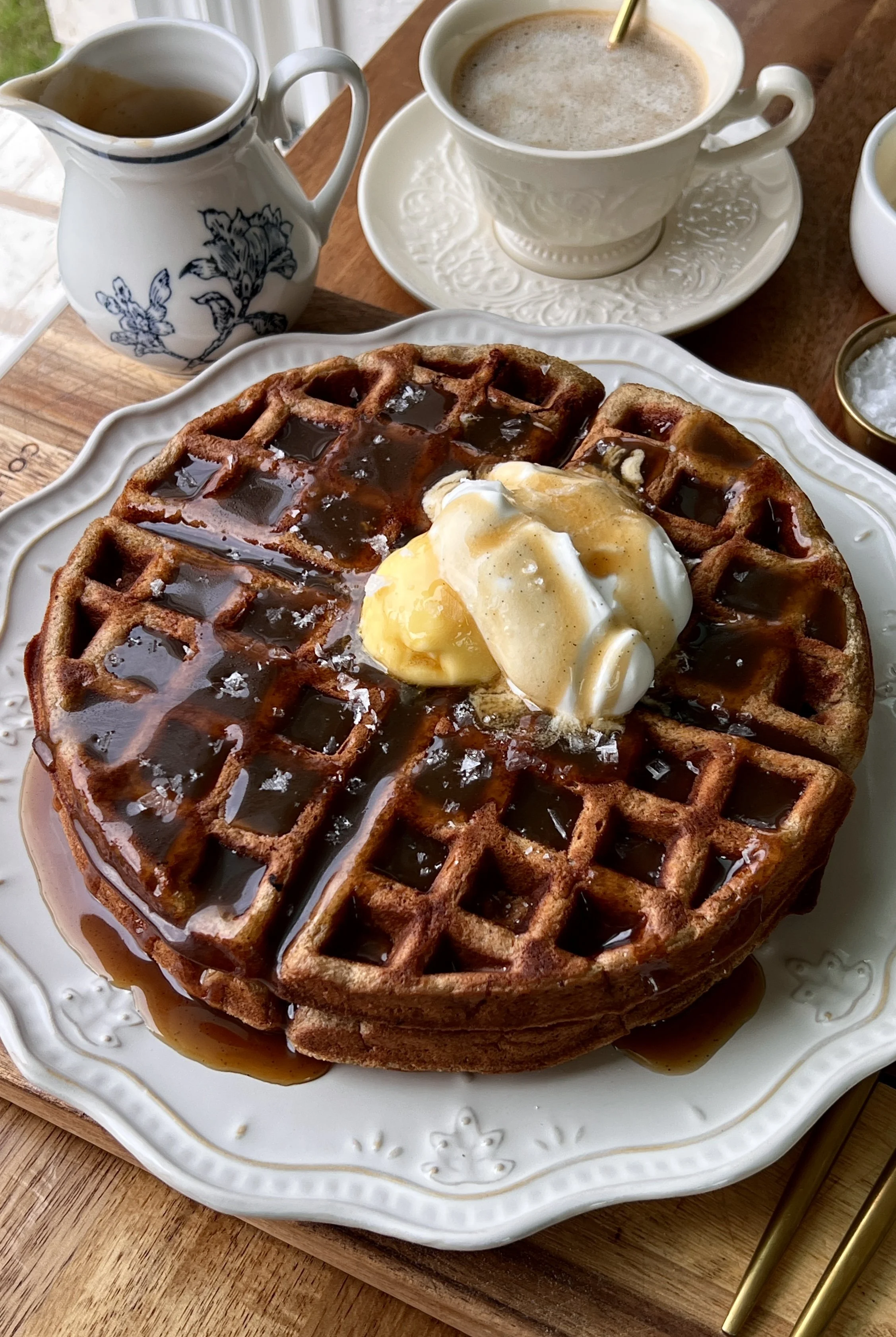 Sticky toffee waffles served warm with butter, whipped sour cream topping, and a drizzle of silky maple toffee sauce with a hot cup of coffee.