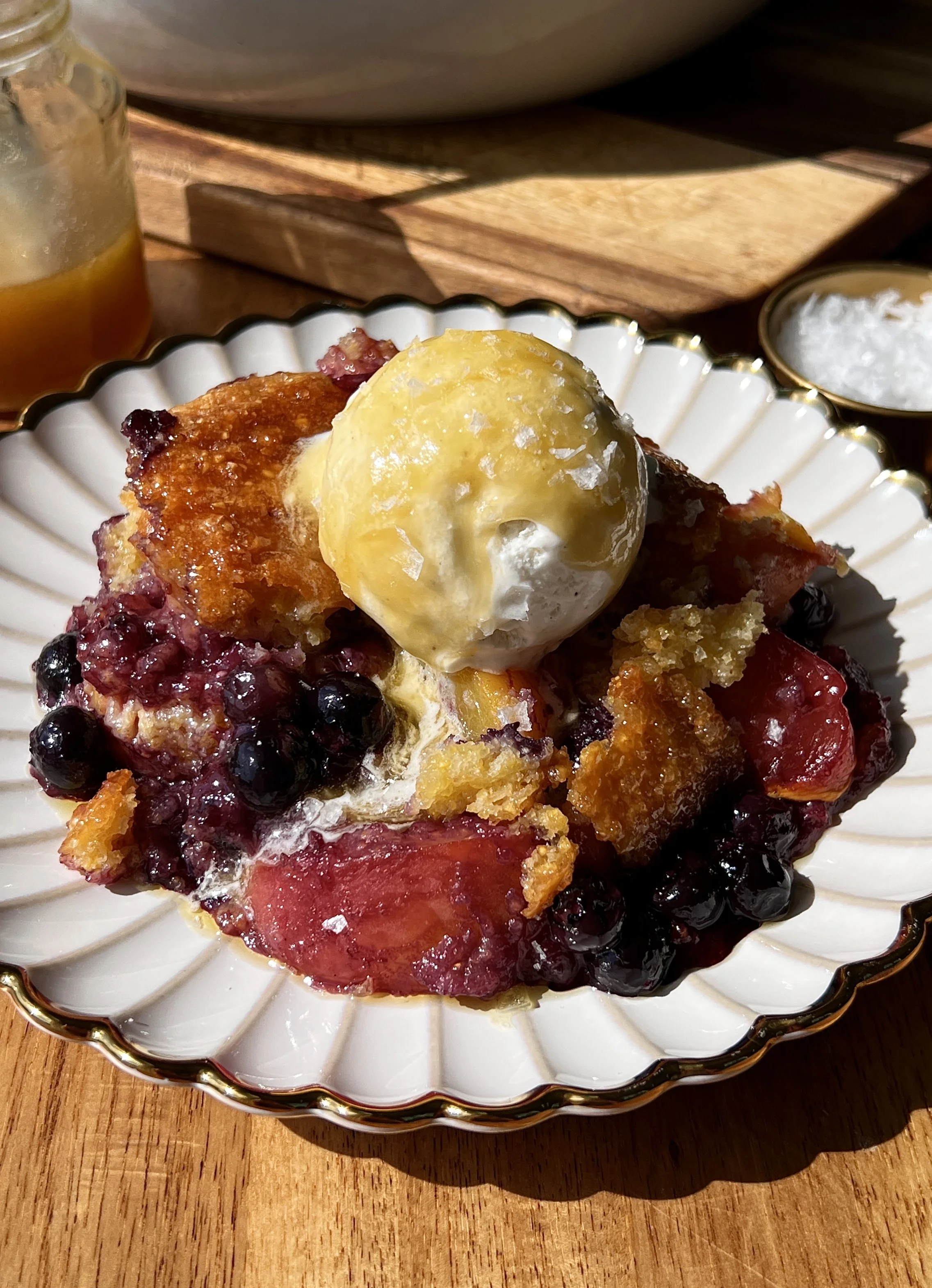 Blueberry peach cornbread cobbler brushed with melted honey butter served warm with a scoop of vanilla ice cream and flaky sea salt.