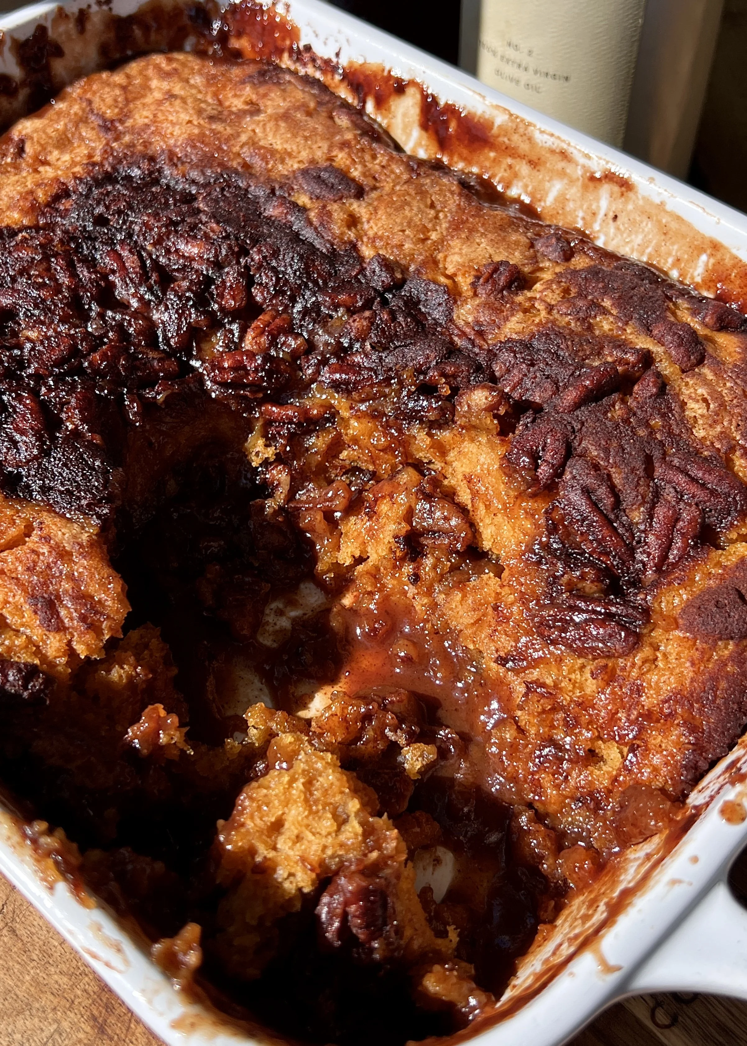 Brown butter sweet potato pecan pudding cake with a scoop taken out showing the golden crisp cake top and warm gooey syrupy bottom served with a scoop of vanilla ice cream and flaky sea salt.
