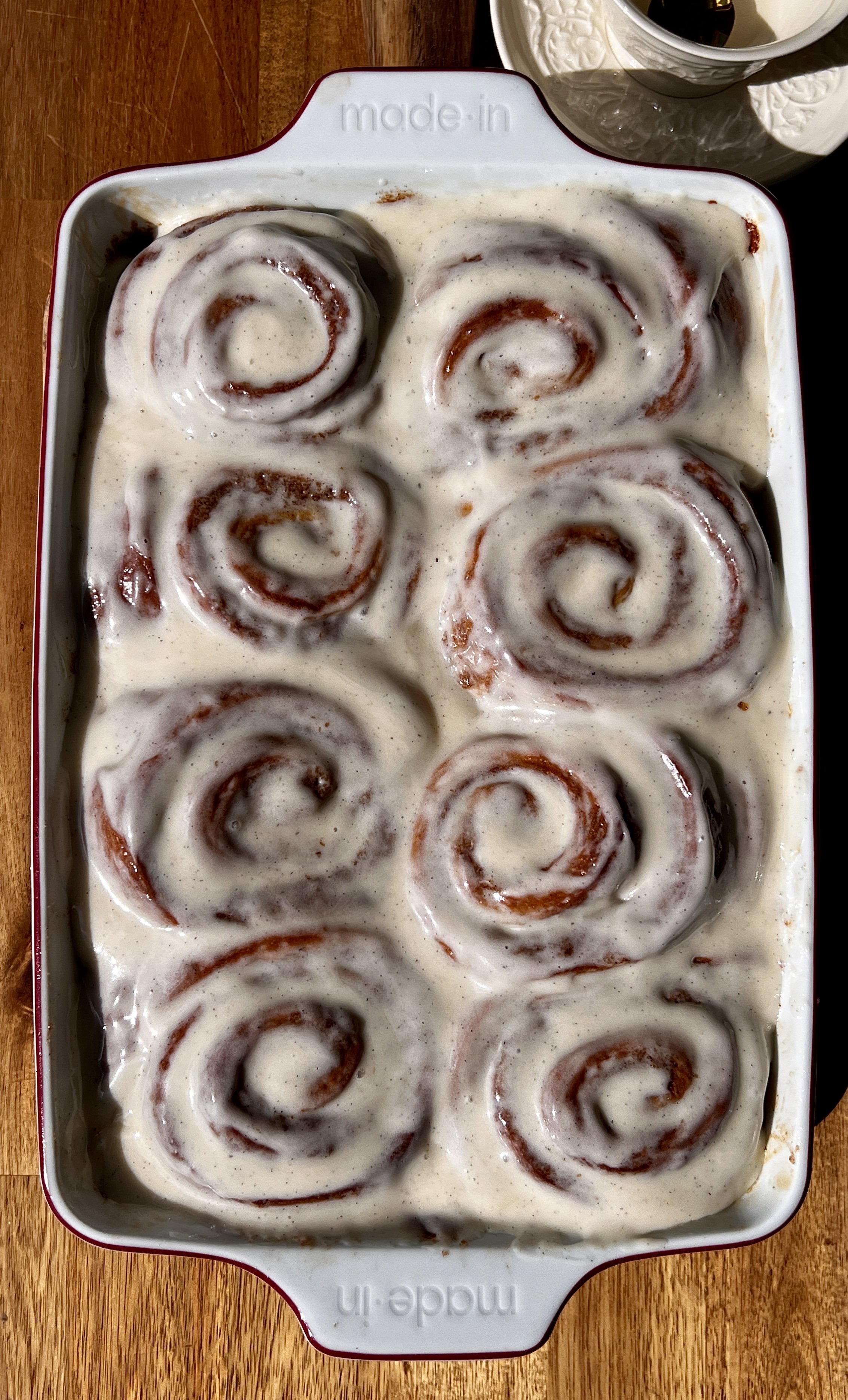 Pan of golden homemade pumpkin cinnamon rolls with sticky caramelized edges and a warming pumpkin spice cinnamon filling topped with classic cream cheese frosting melting into every swirl.