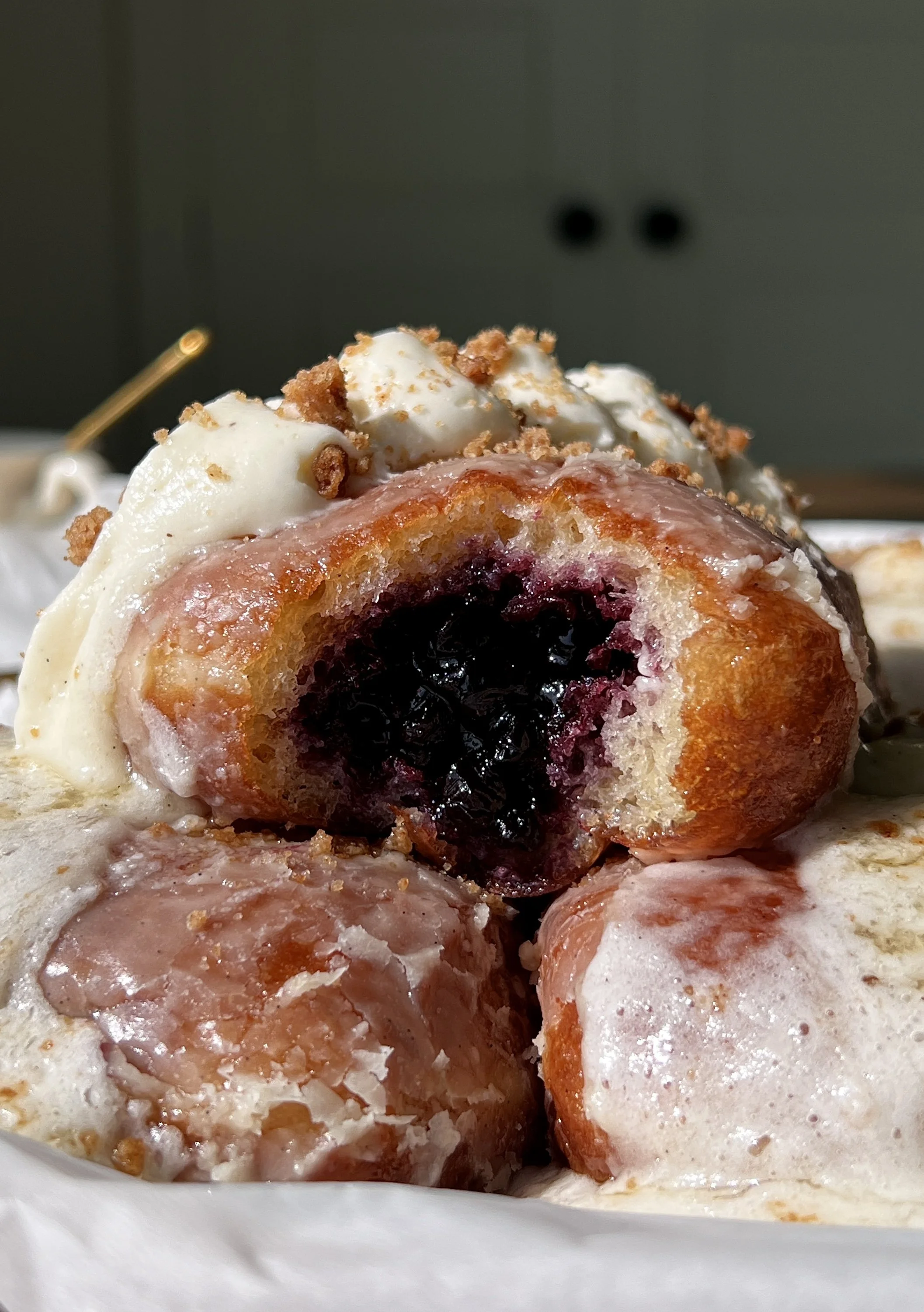 Blueberry pie donut bar with a bite taken out showing the homemade blueberry compote filling inside coated in a vanilla bean glaze with whipped buttercream and shortbread crumbles on top.