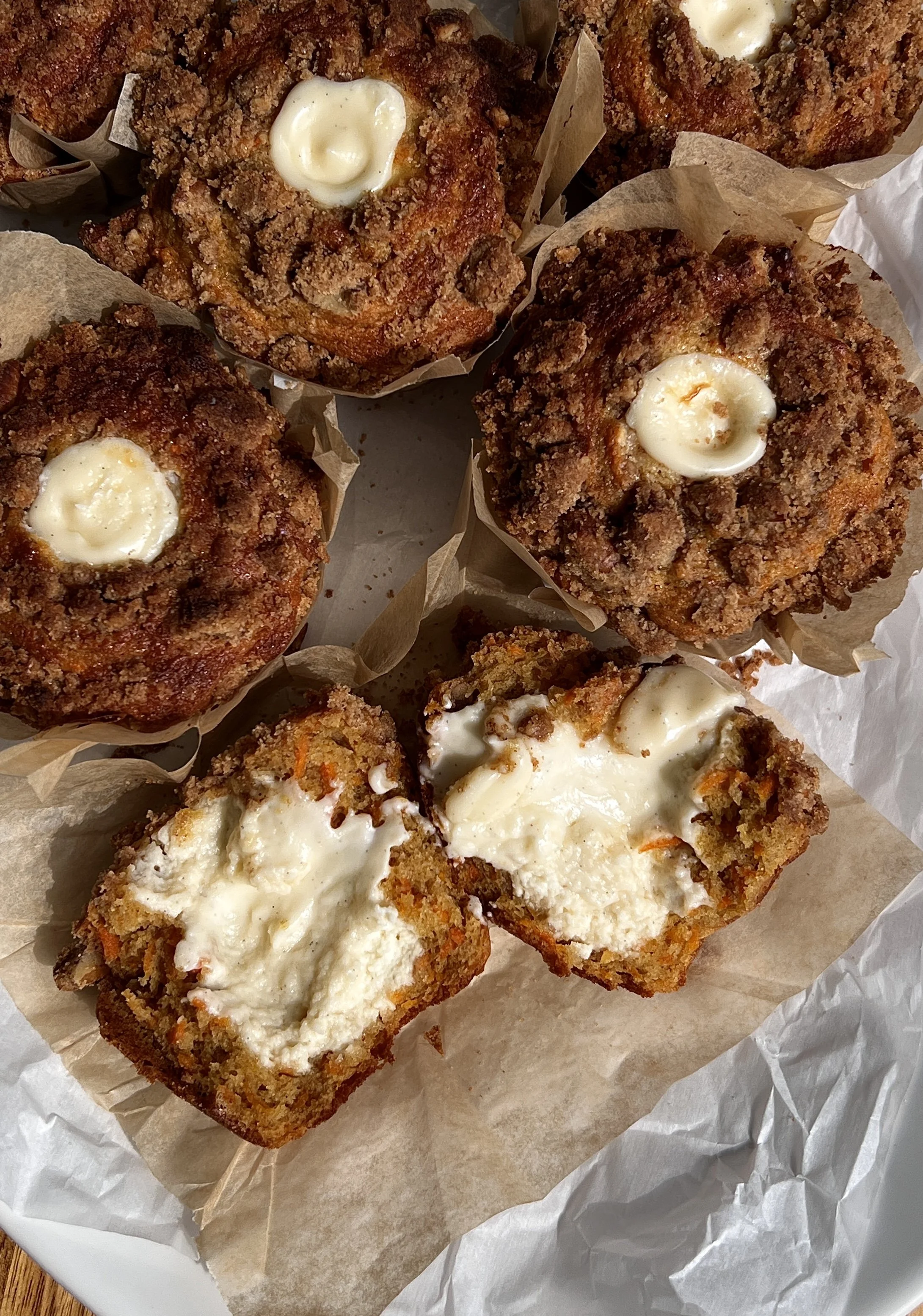 Carrot cake muffin broken open showing soft crumb and creamy cream cheese center.