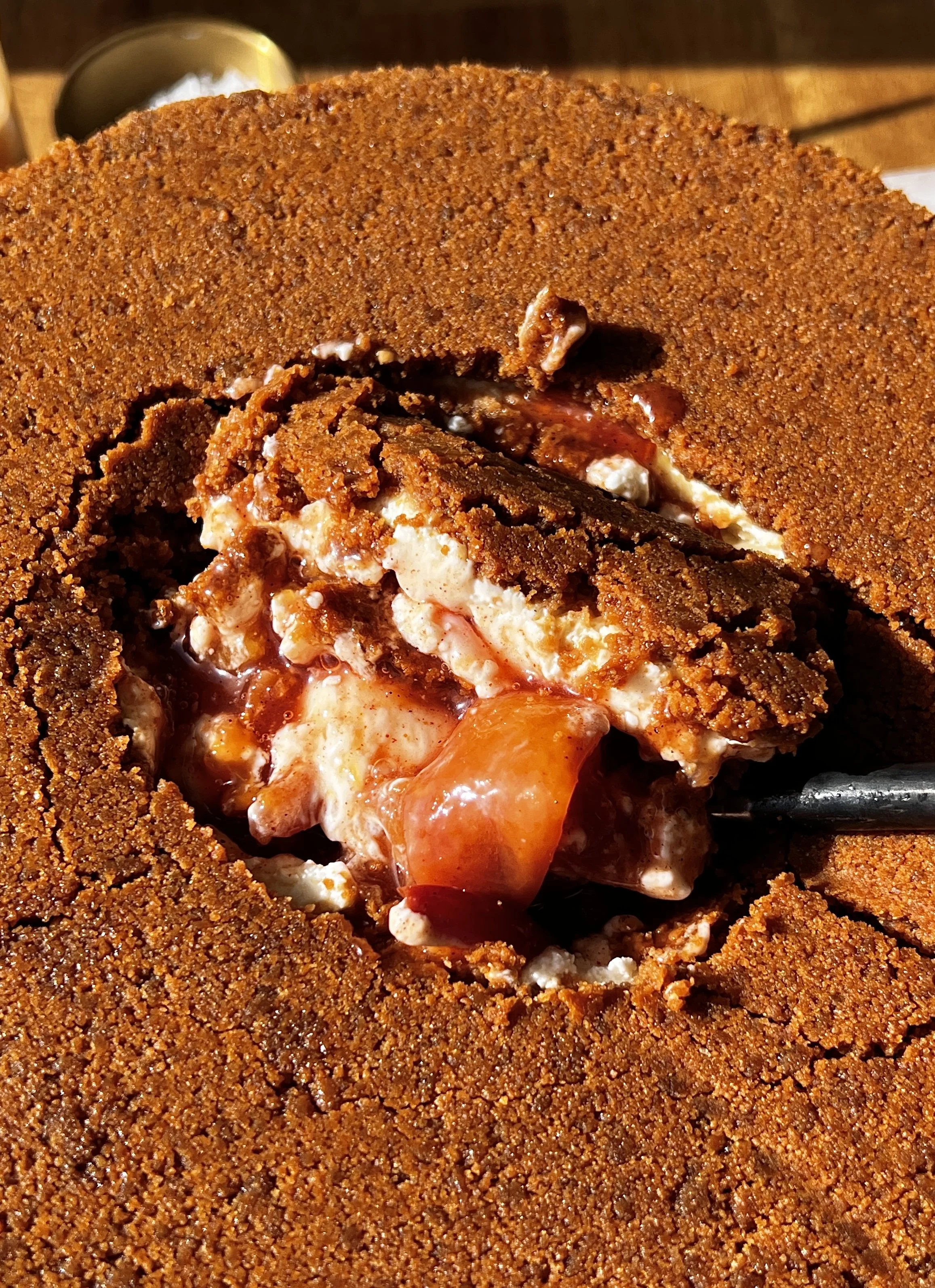 Fully crusted upside down peach cobbler cheesecake being smashed into with a spoon revealing the rich and creamy no-bake cheesecake filling and sweet jammy homemade peach filling inside.