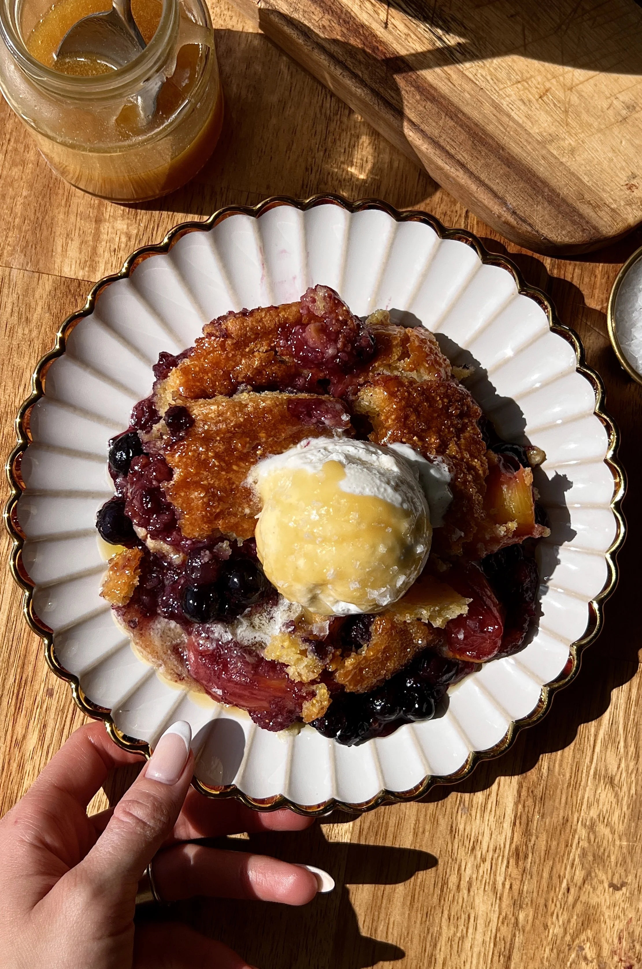 Warm and golden blueberry peach cornbread cobbler brushed with melted honey butter served with a scoop of vanilla ice cream, an extra drizzle of honey butter, and a sprinkle of flaky sea salt as the ultimate summer dessert.