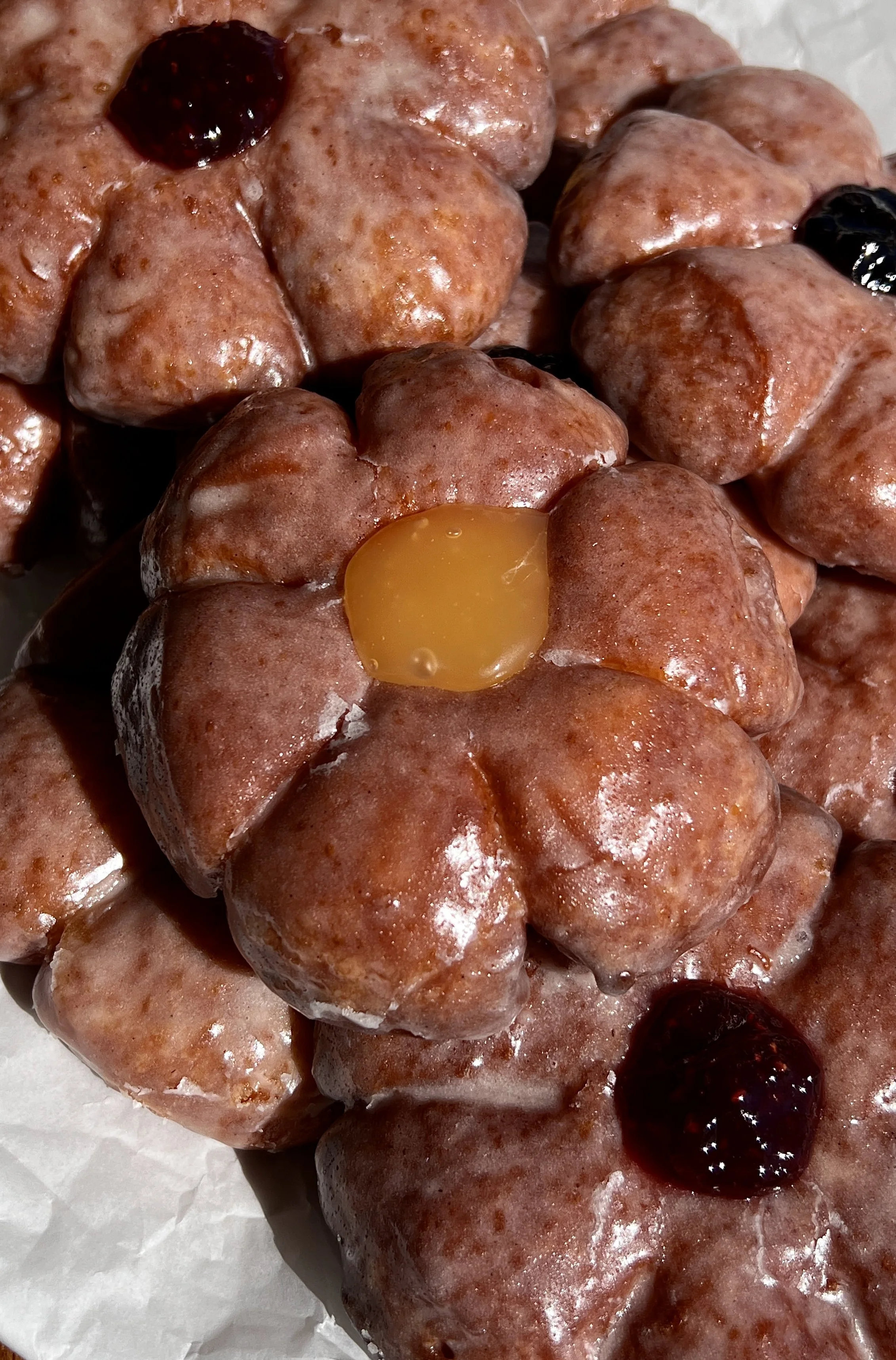 Close-up of flower donuts with soft, fluffy centers and golden, slightly chewy edges coated in glaze.
