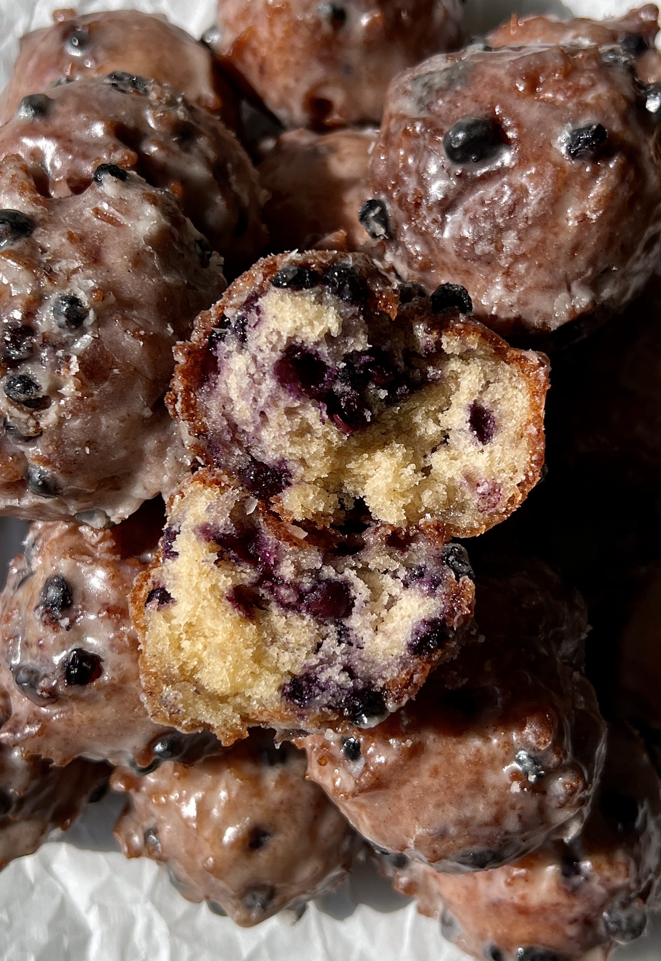Close-up of a soft and tender sourdough blueberry fritter bite with a beautifully golden exterior coated in a silky vanilla bean glaze with bright juicy blueberries throughout.