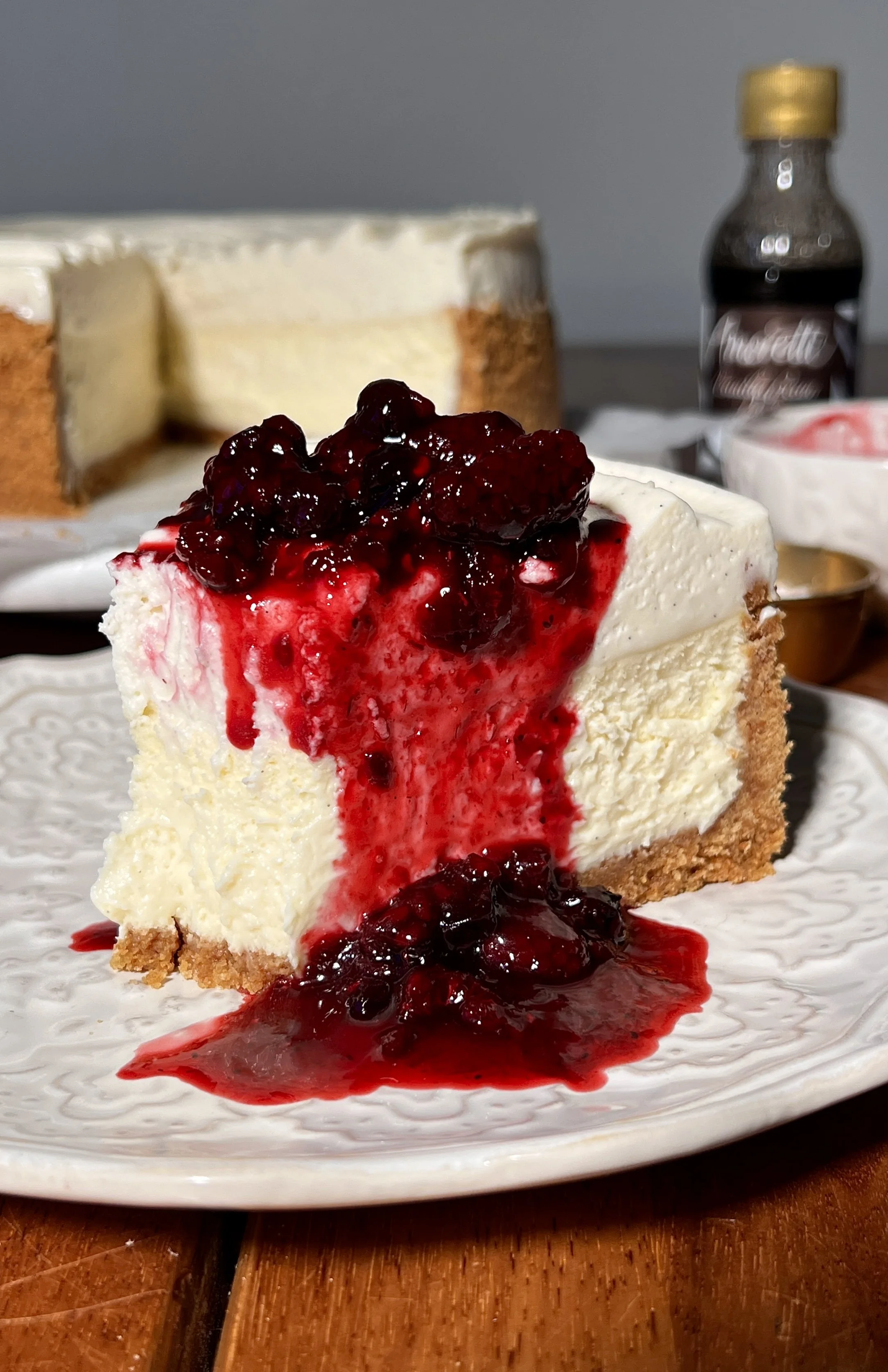 Creamy vanilla bean cheesecake with a buttery graham cracker crust, topped with a smooth layer of white chocolate mousse and finished with a glossy berry compote on top.