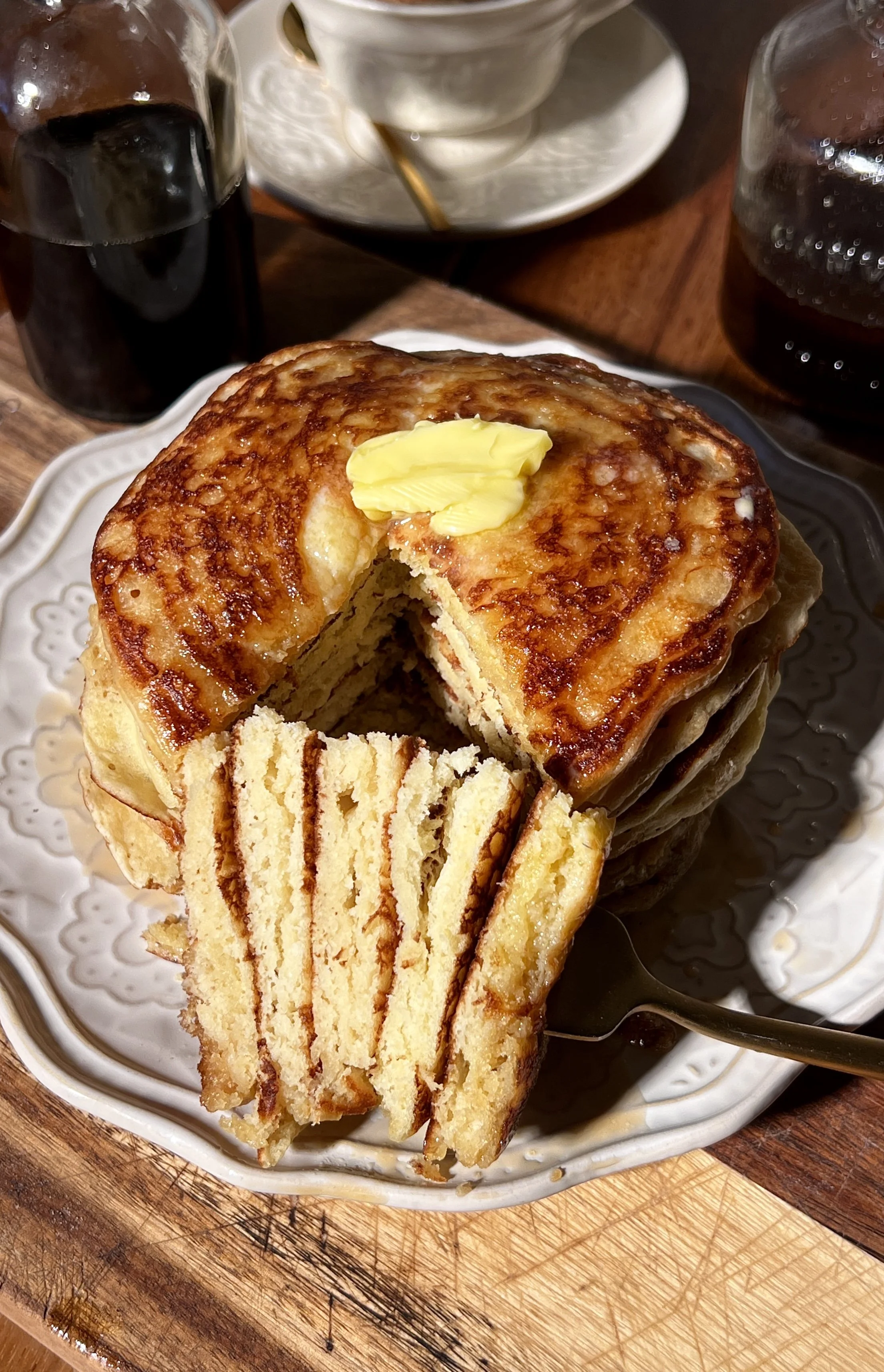 Classic buttermilk pancakes stacked high on a plate, soft and fluffy with golden edges, topped with butter and maple syrup, served alongside a warm maple brown butter latte.