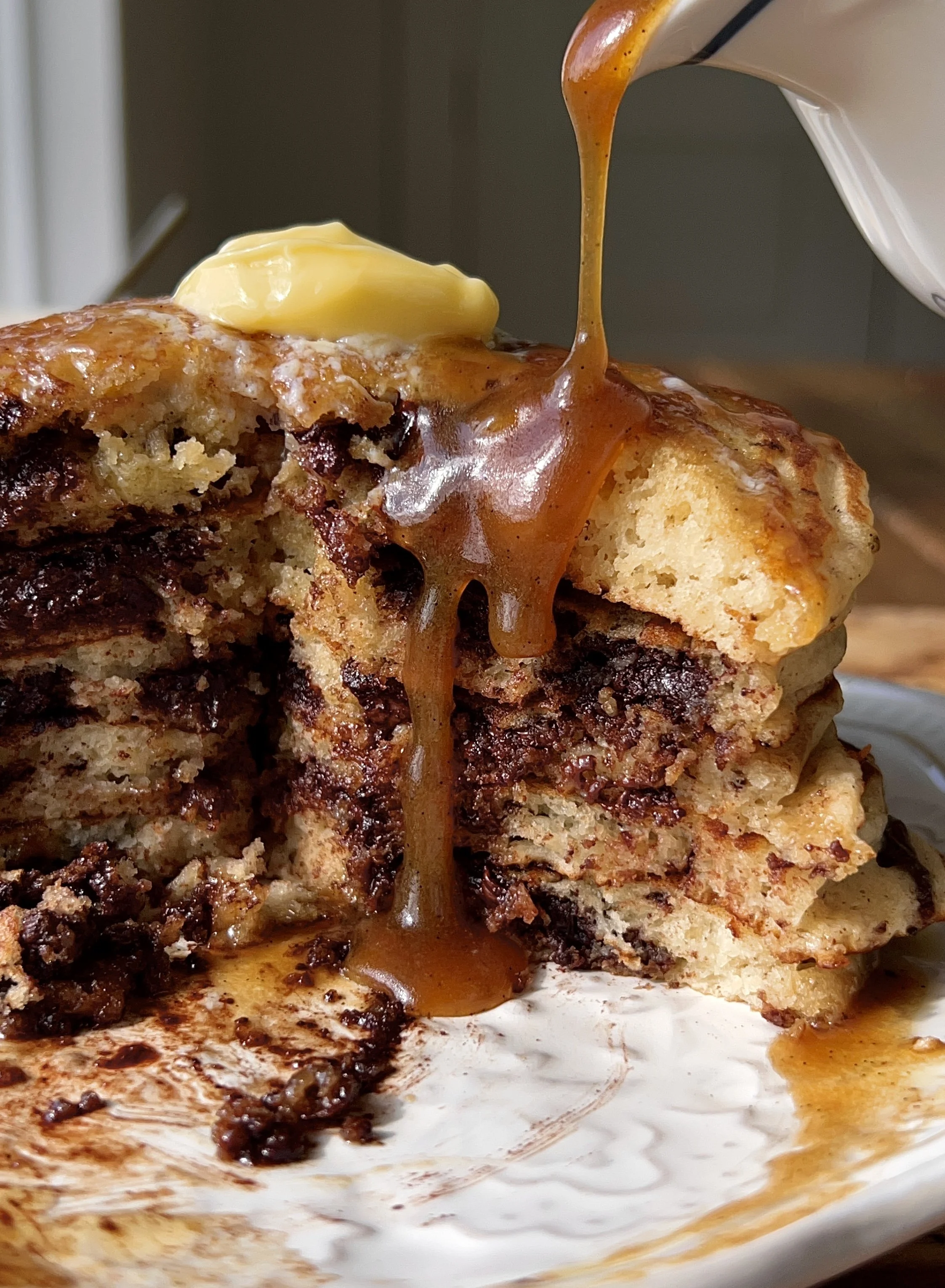 Soft and fluffy brown butter chocolate chip pancakes served warm with a pat of butter, maple espresso buttermilk syrup, and a hot cup of coffee.