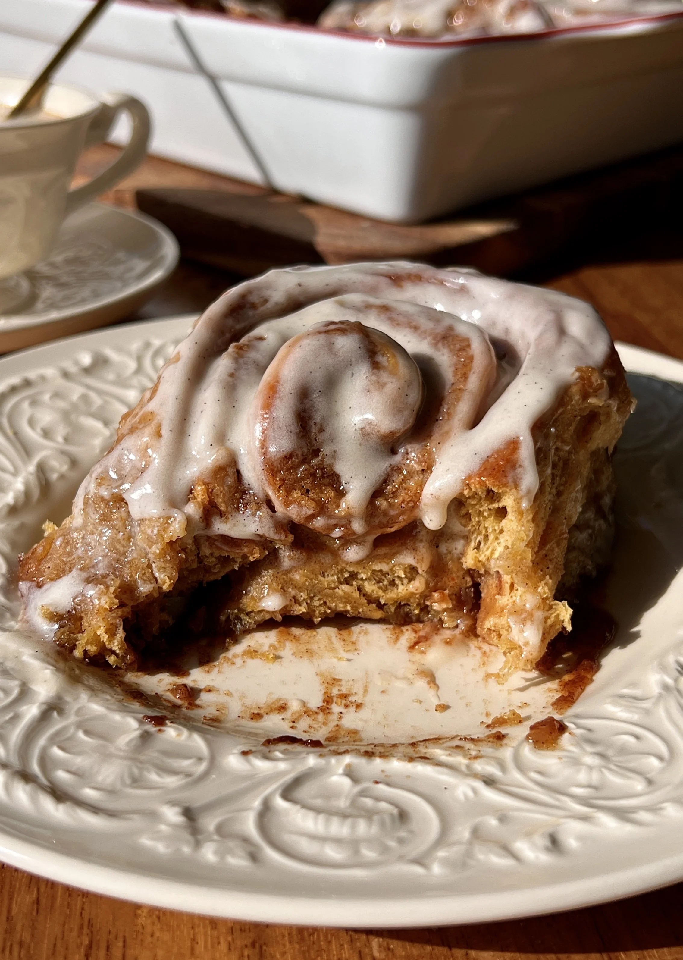 Close-up of a soft and fluffy homemade pumpkin cinnamon roll with beautifully golden caramelized edges and a warming gooey pumpkin spice cinnamon filling with cream cheese frosting melting into every swirl.