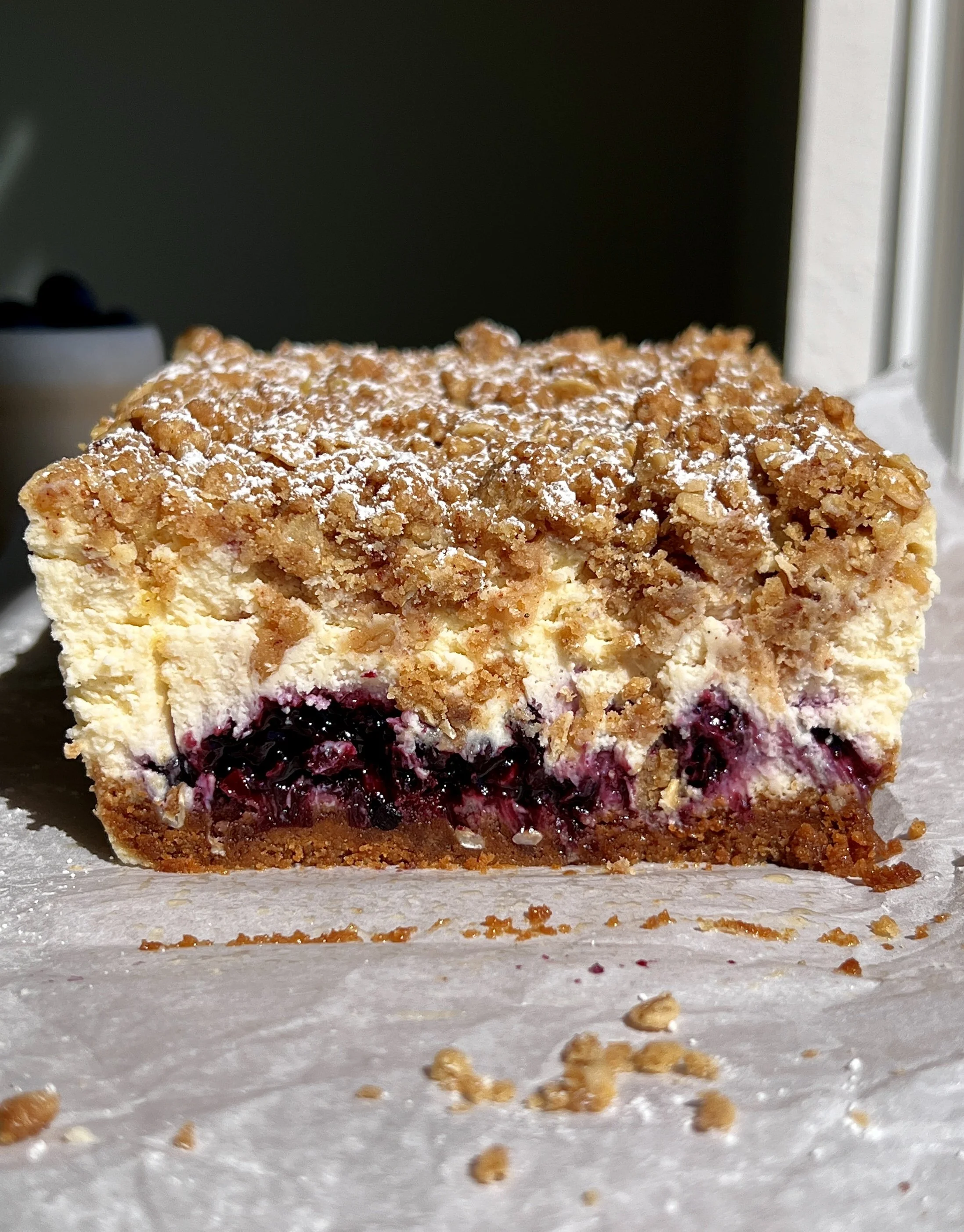 Close-up of a blueberry crumble cheesecake bar with pockets of homemade blueberry compote and a golden crumble topping throughout.