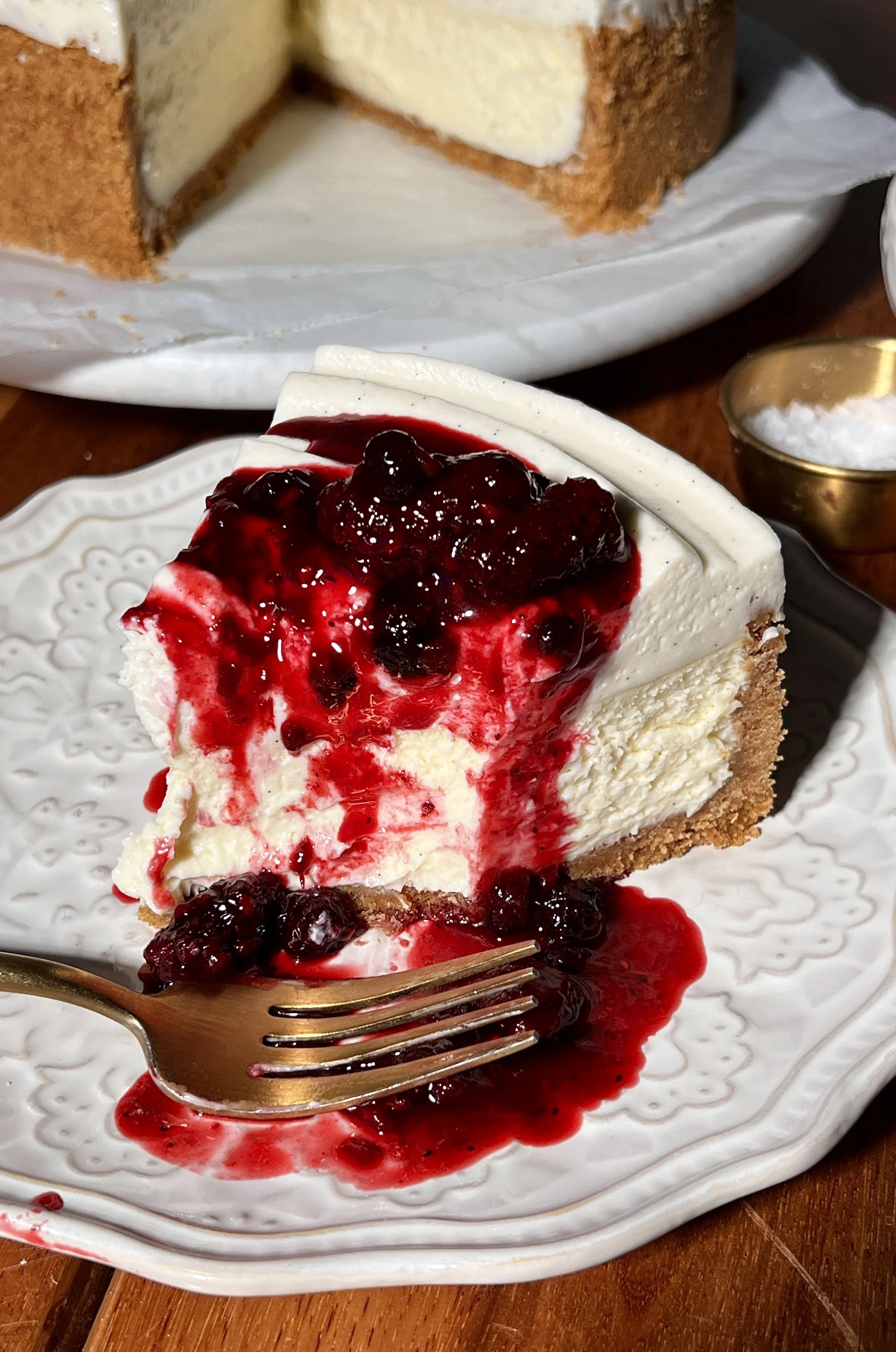 Creamy vanilla bean cheesecake with a buttery graham cracker crust, topped with a smooth layer of white chocolate mousse and finished with a glossy berry compote on top.