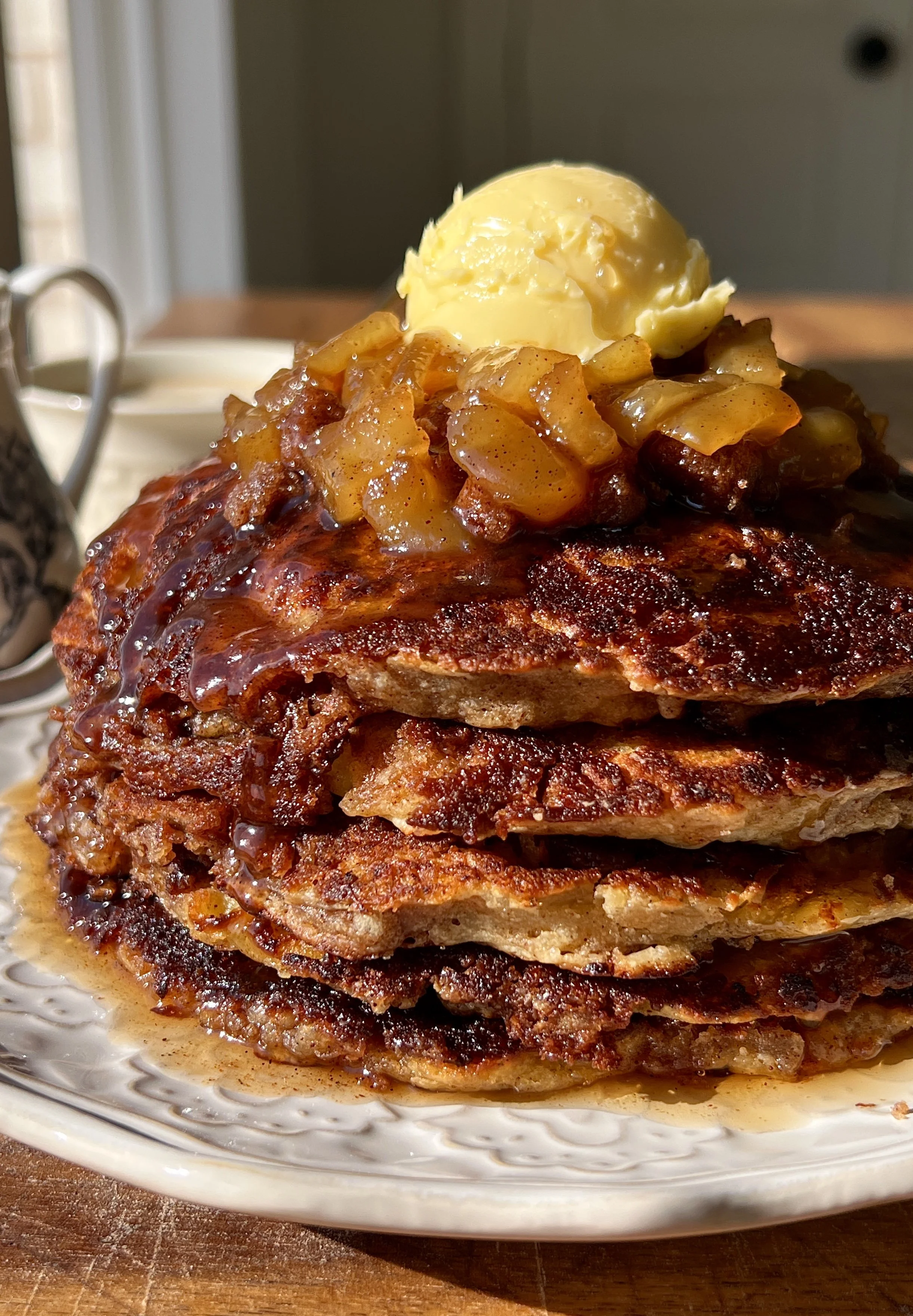 Stack of golden apple streusel griddle cakes with crisp edges, warm gooey apple filling, and caramelized cinnamon streusel served warm with a pat of butter, a drizzle of maple syrup, and a hot cup of coffee.