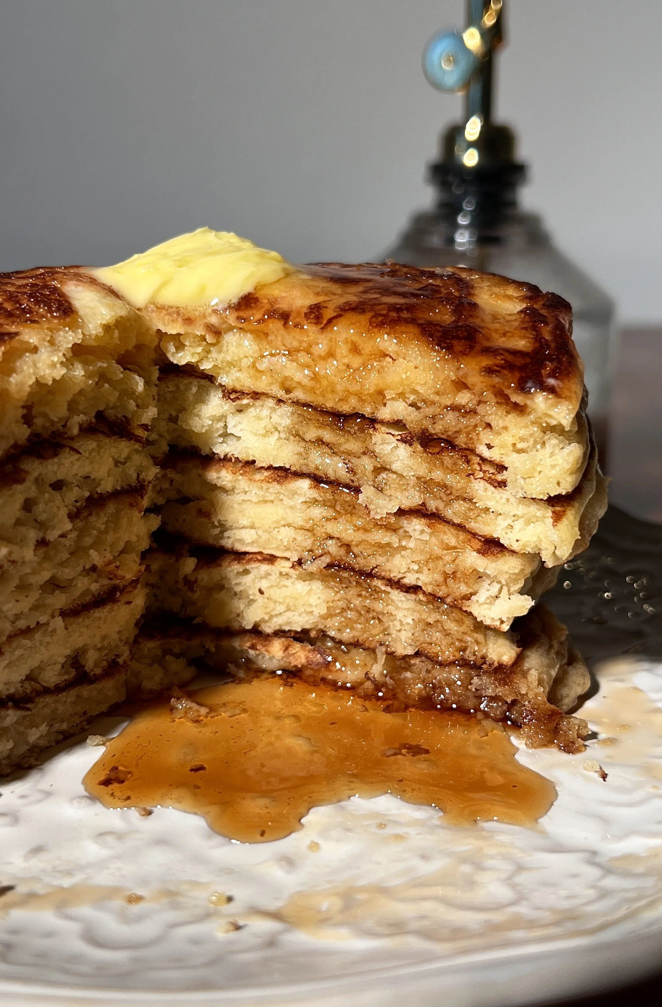 Classic buttermilk pancakes stacked high on a plate, soft and fluffy with golden edges, topped with butter and maple syrup, served alongside a warm maple brown butter latte.