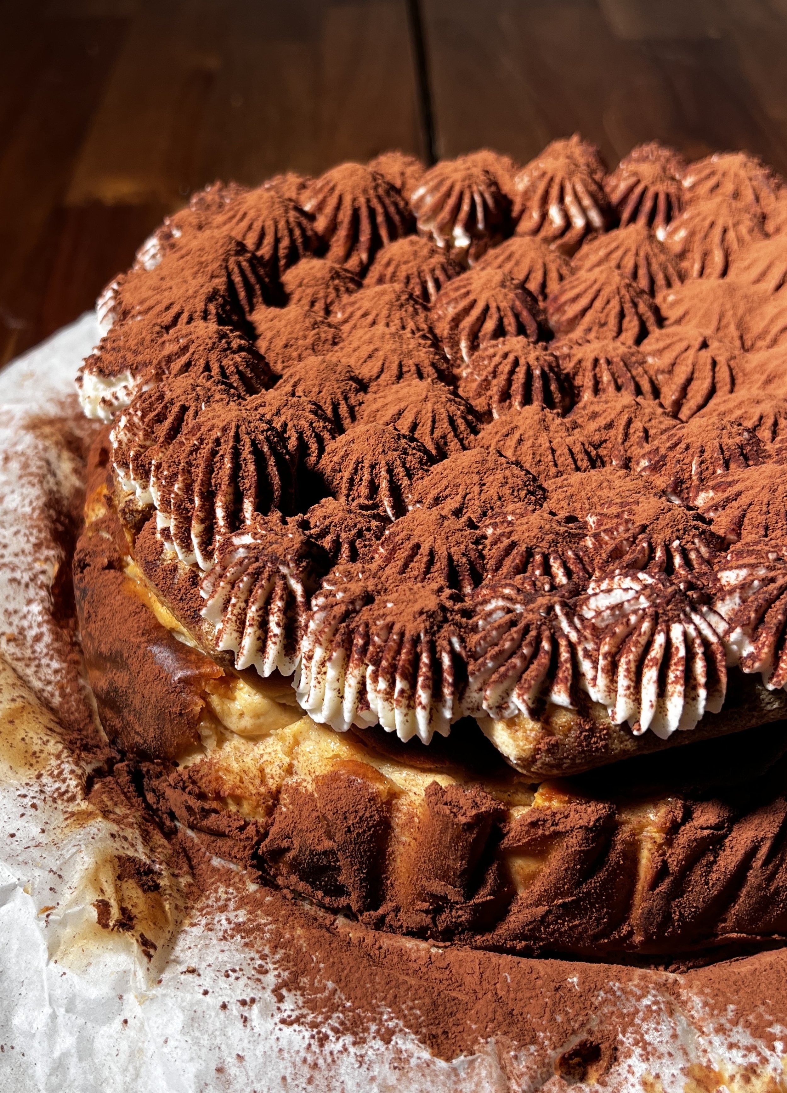 Tiramisu basque cheesecake topped with espresso-soaked ladyfingers, creamy mascarpone layer, and a generous dusting of cocoa powder.