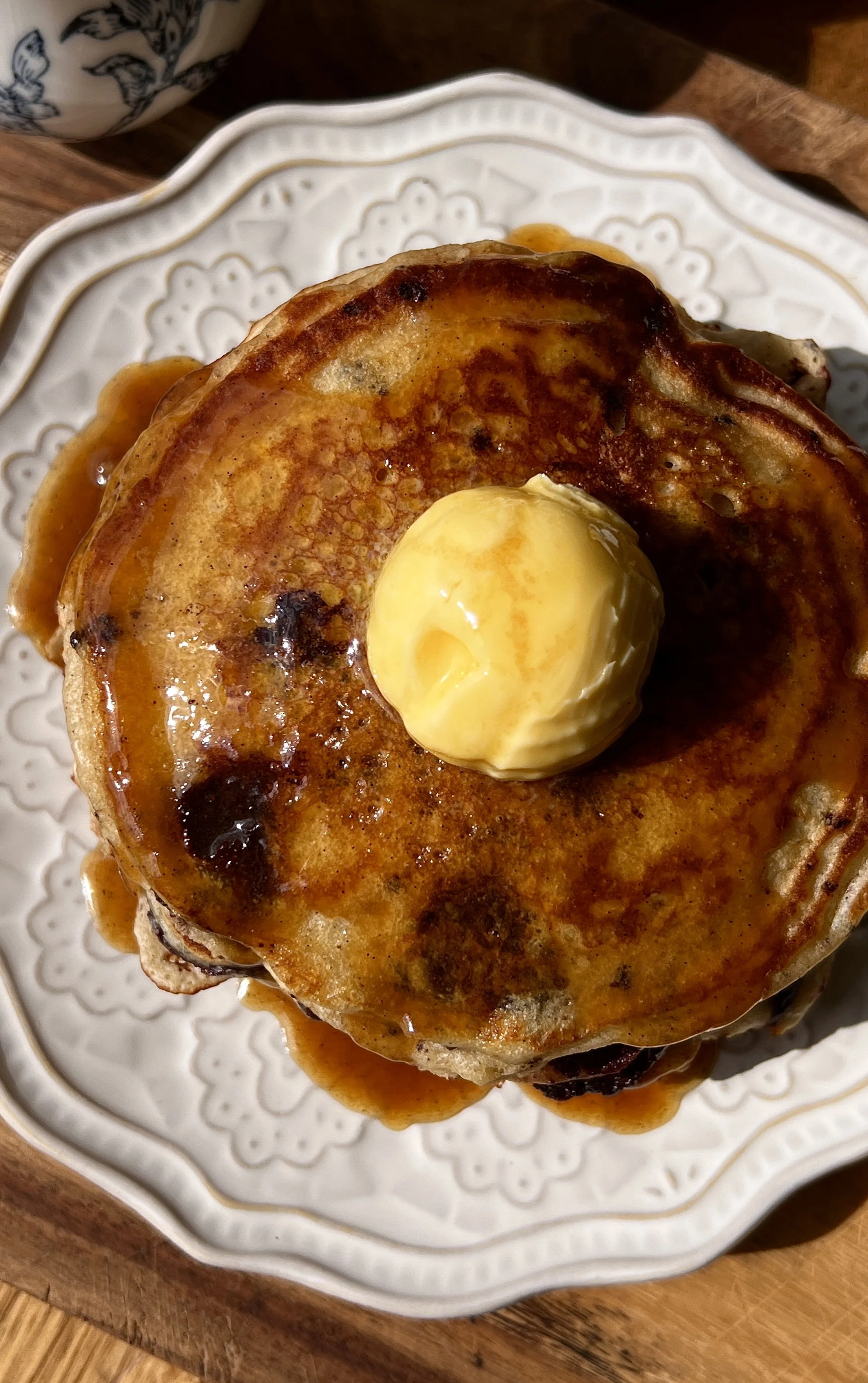 Soft and fluffy brown butter chocolate chip pancakes served warm with a pat of butter, maple espresso buttermilk syrup, and a hot cup of coffee.