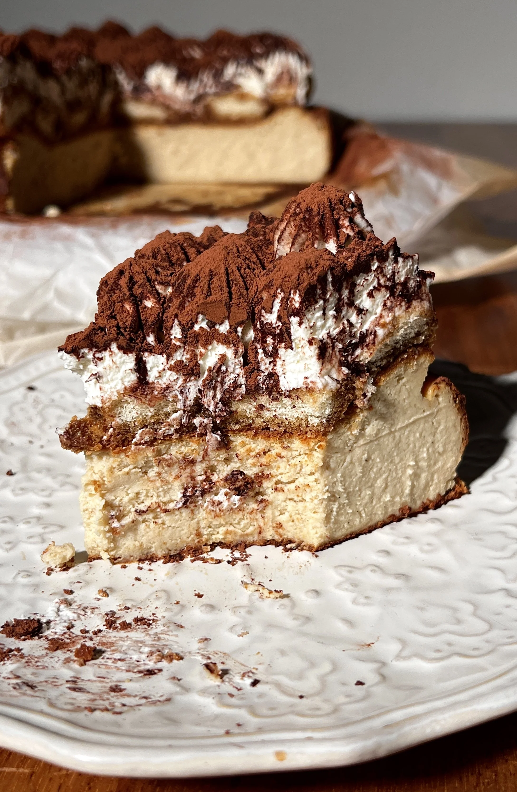 Tiramisu basque cheesecake topped with espresso-soaked ladyfingers, creamy mascarpone layer, and a generous dusting of cocoa powder.